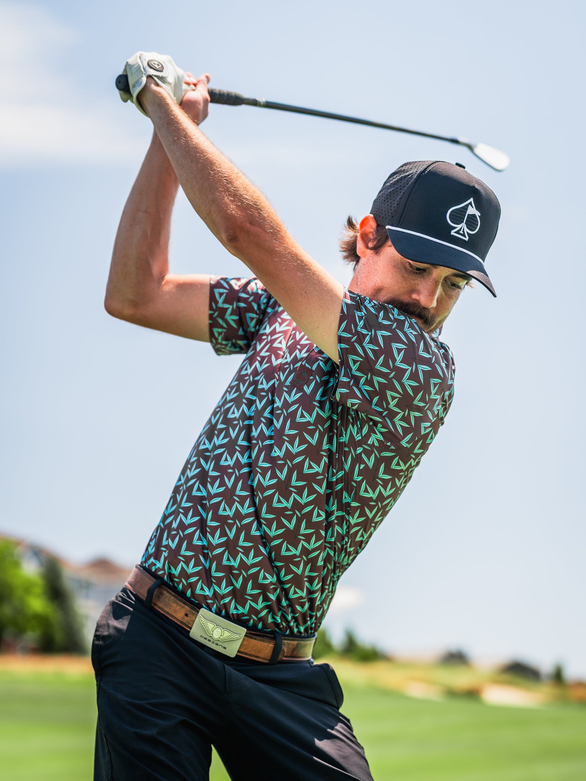Bold golfer wearing the Cocoa Verde shirt, featuring a unique geometric pattern, swinging a golf club on the course.