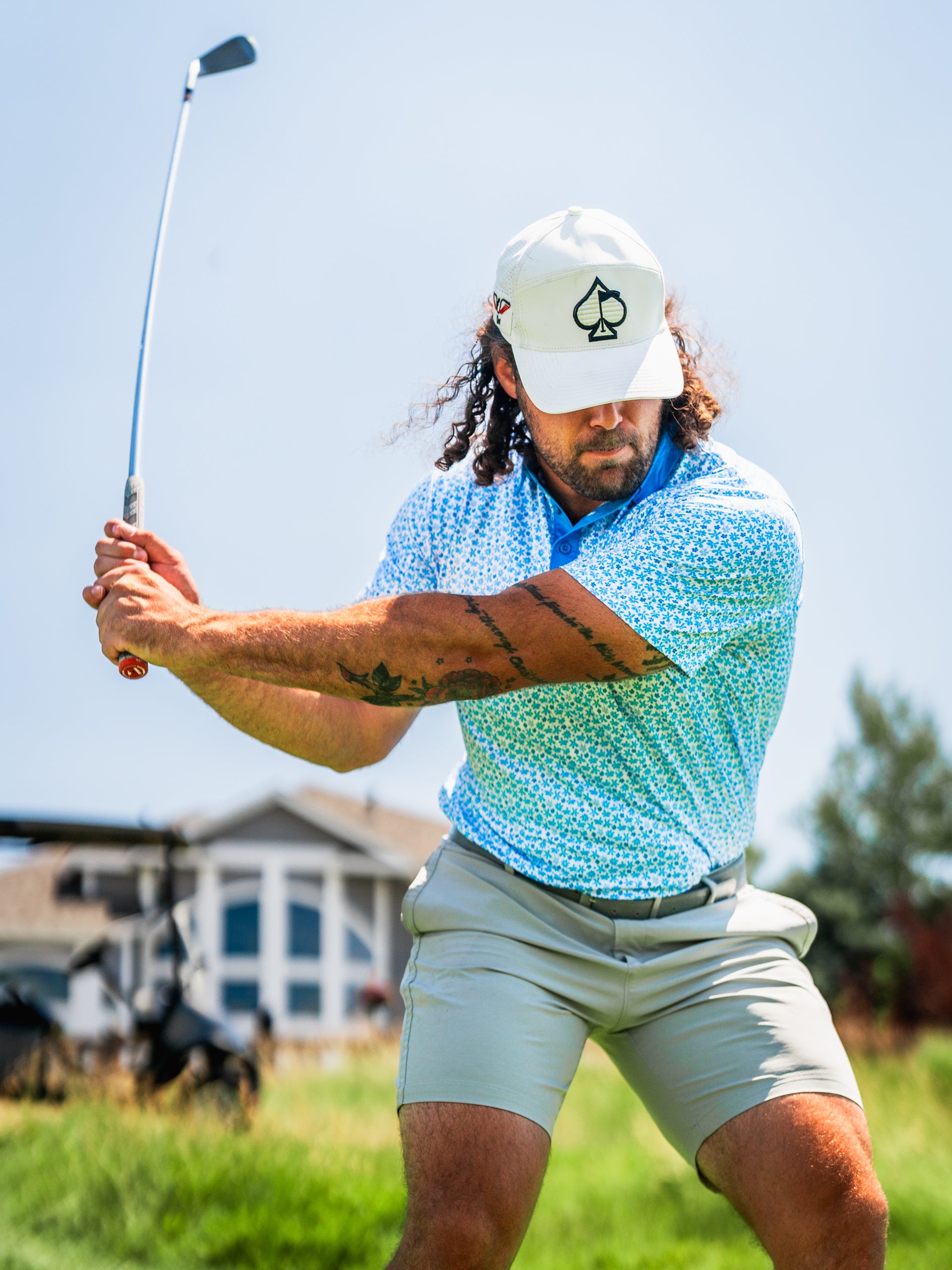 A golfer swings a club while wearing a floral-patterned shirt and a cap, showcasing a stylish and bold golf look.