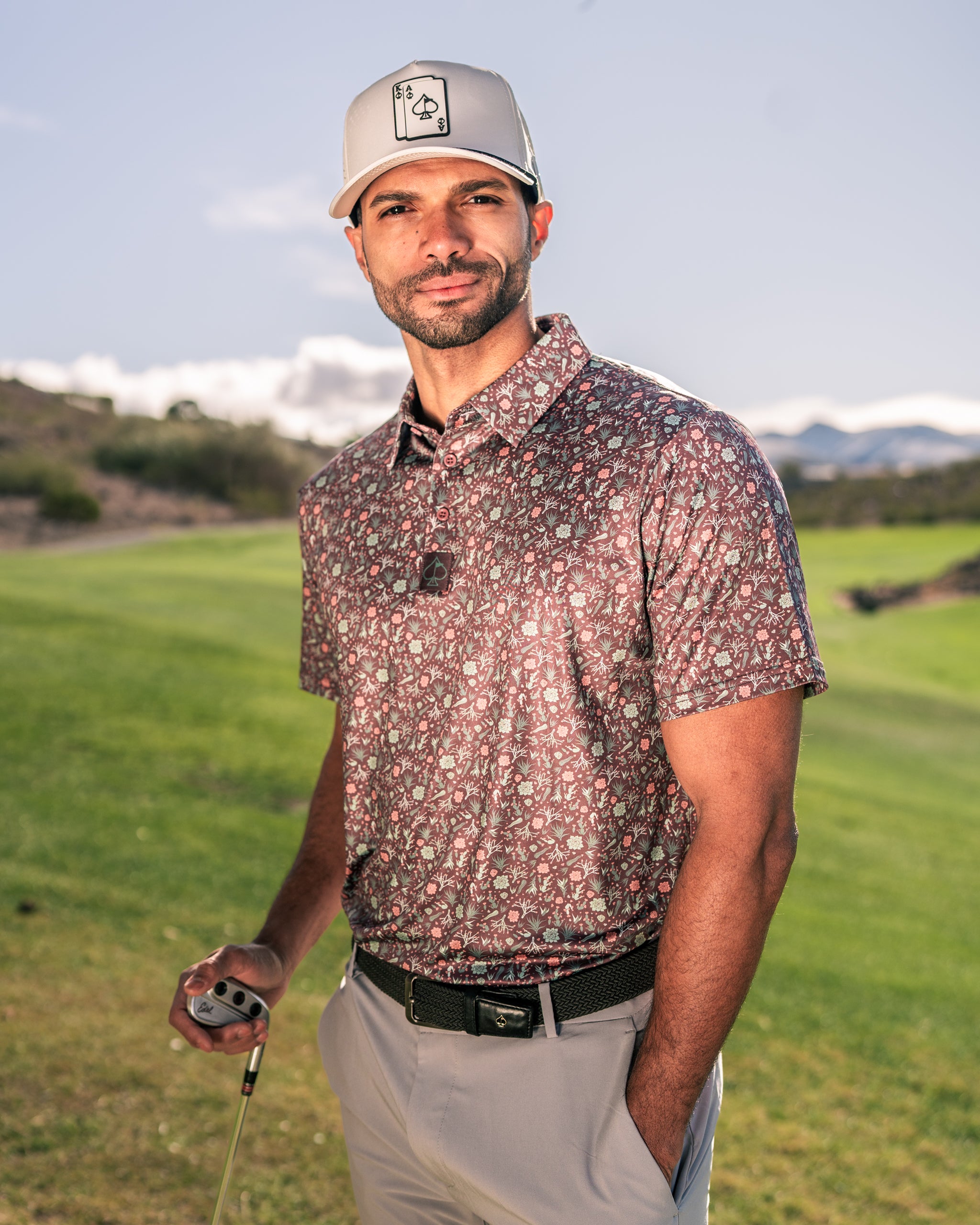 Stylish golfer wearing a Desert Sage patterned polo shirt and cap, posing on a lush green golf course.