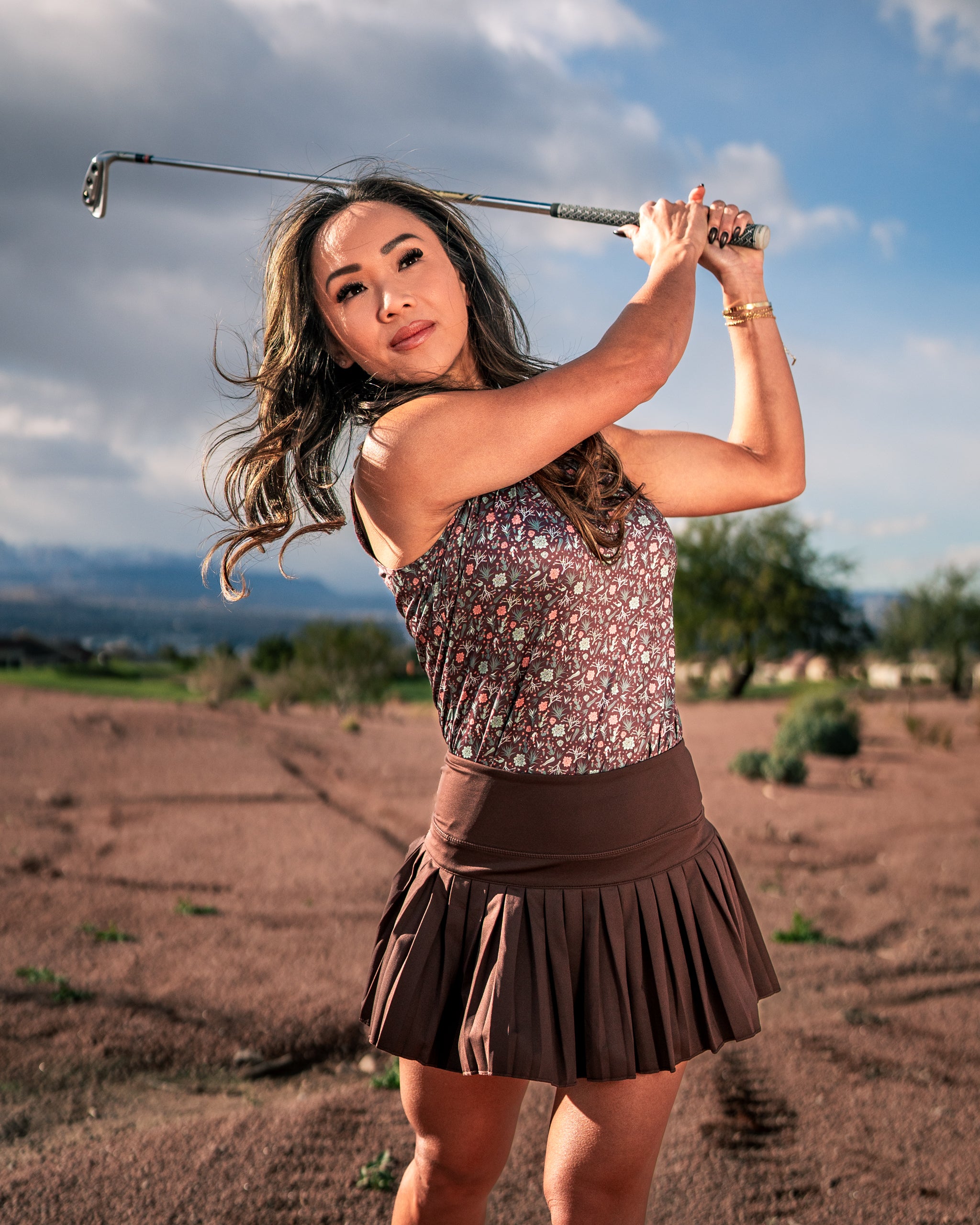 Women's Desert Sage golf outfit featuring a floral top and brown pleated skirt, perfect for stylish performance on the course.