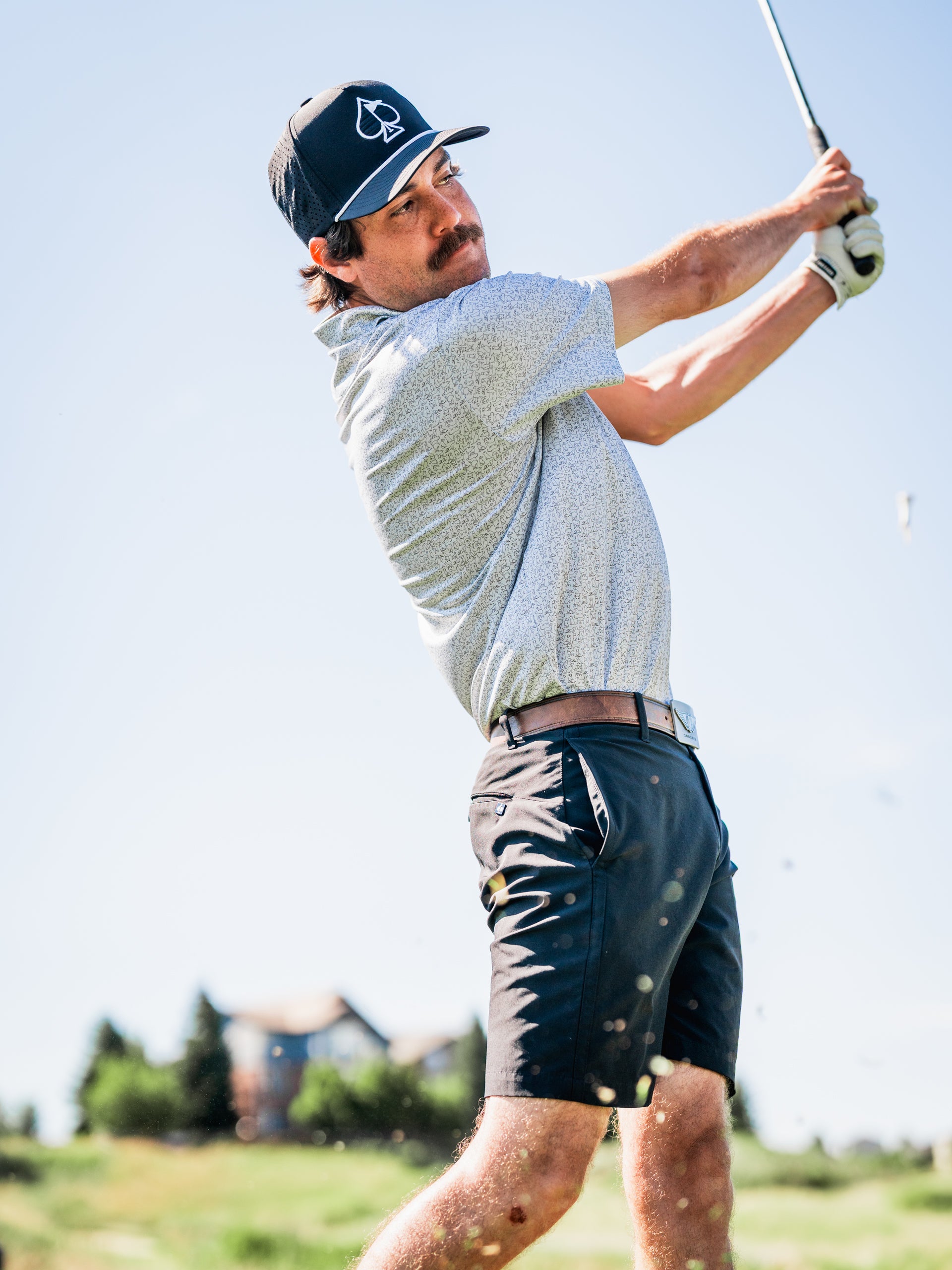 A golfer swings a club on the course, wearing a stylish shirt and shorts, showcasing bold golf apparel.