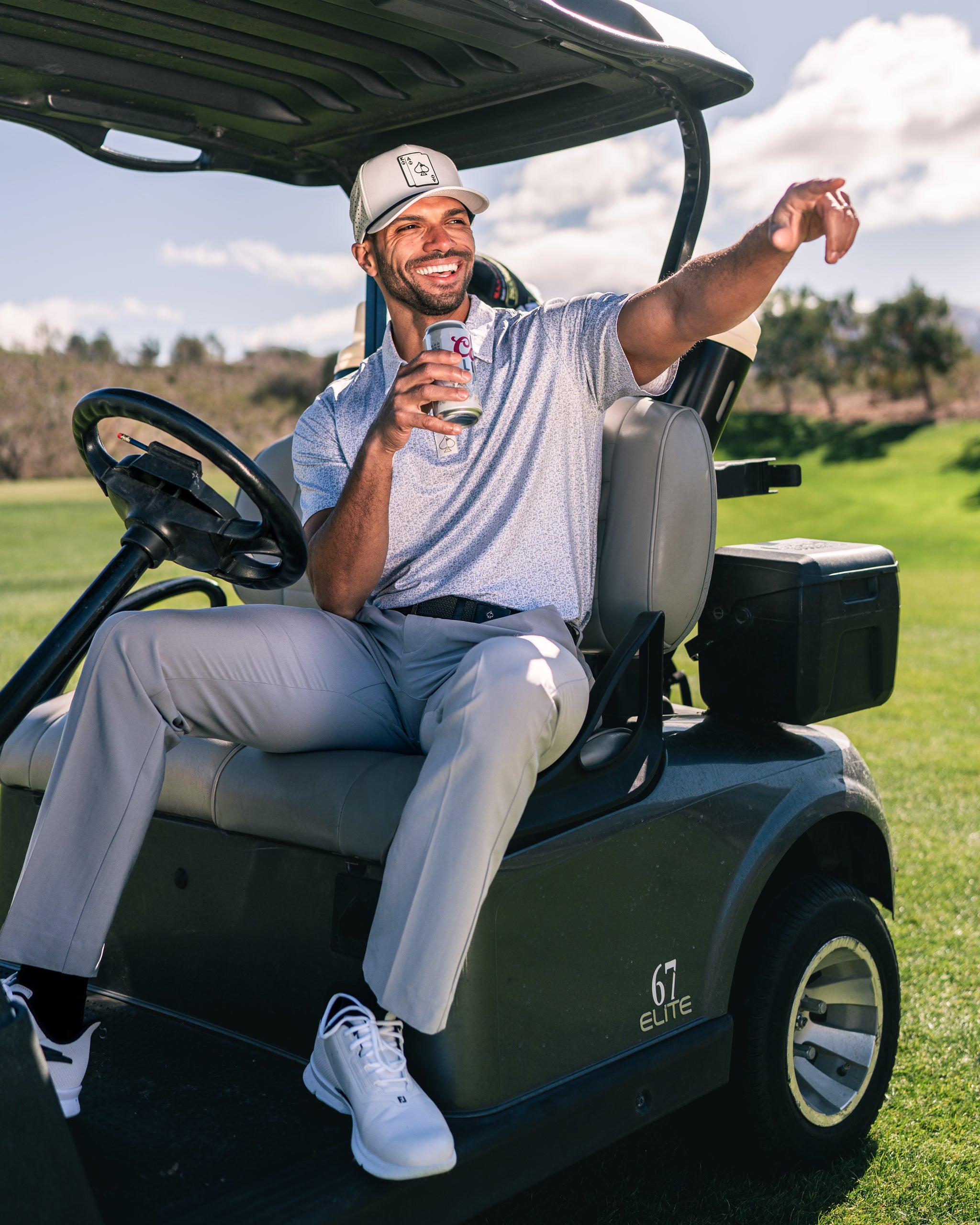 A golfer relaxes on a golf cart, wearing a stylish polo and cap, enjoying a drink on a sunny course.