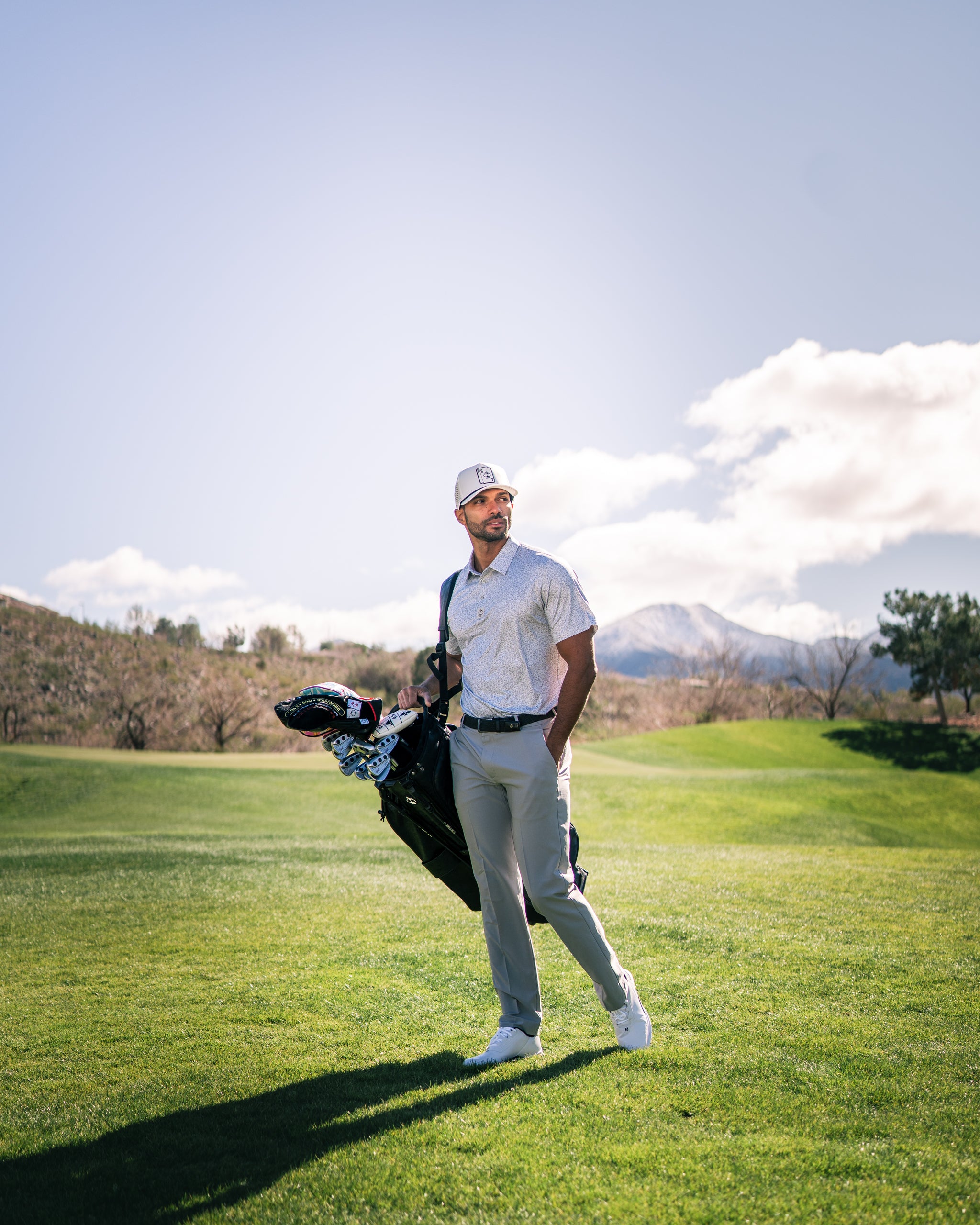 A golfer stands on a sunny course, holding a golf bag with a colorful headcover, dressed in stylish golf apparel.