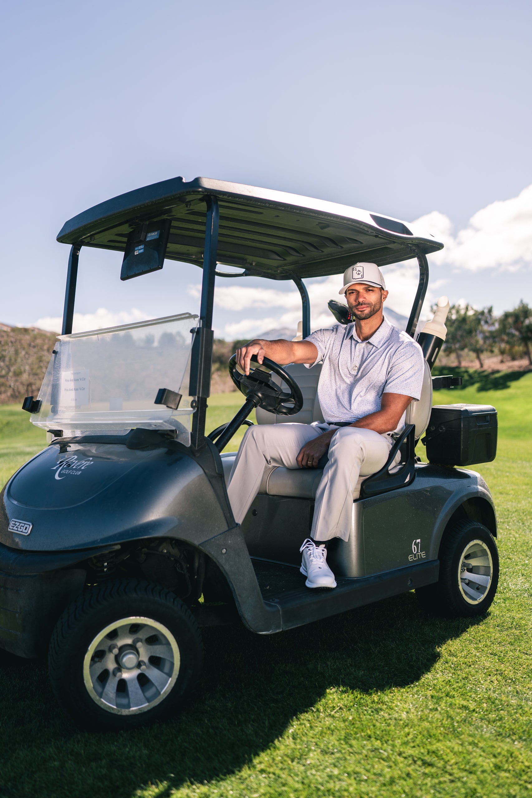 A golfer sits confidently in a golf cart on the course, wearing stylish golf apparel and a cap, ready for a round.