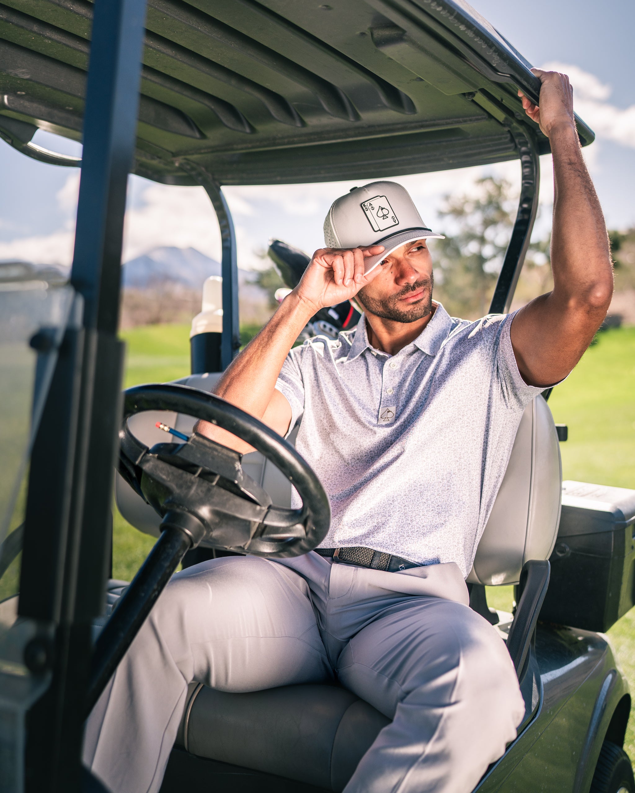 A golfer wearing a stylish cap sits in a golf cart, enjoying a sunny day on the course, showcasing a relaxed vibe.