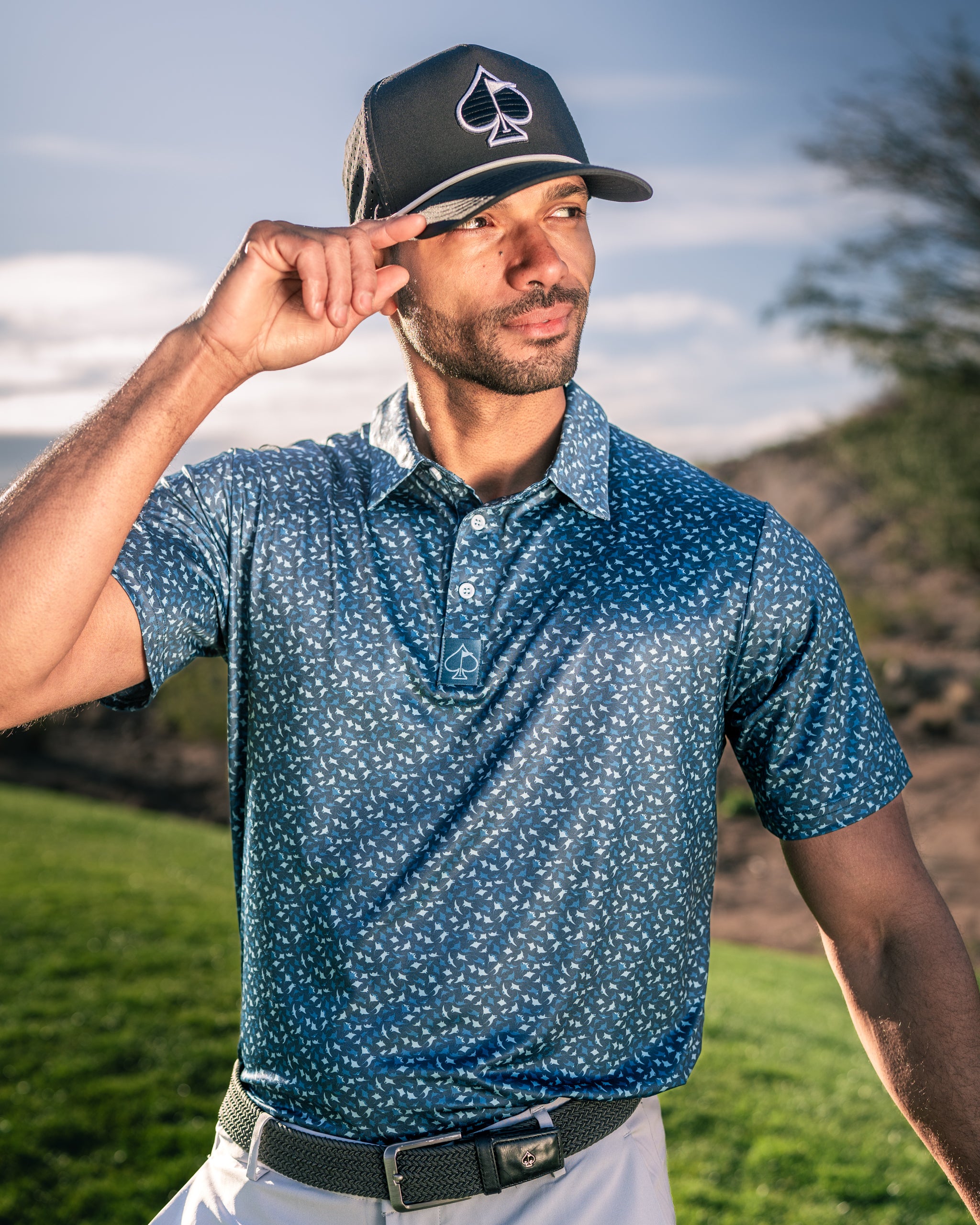 Stylish golfer wearing a blue Manta Ray polo shirt and a cap, posing confidently on the golf course.