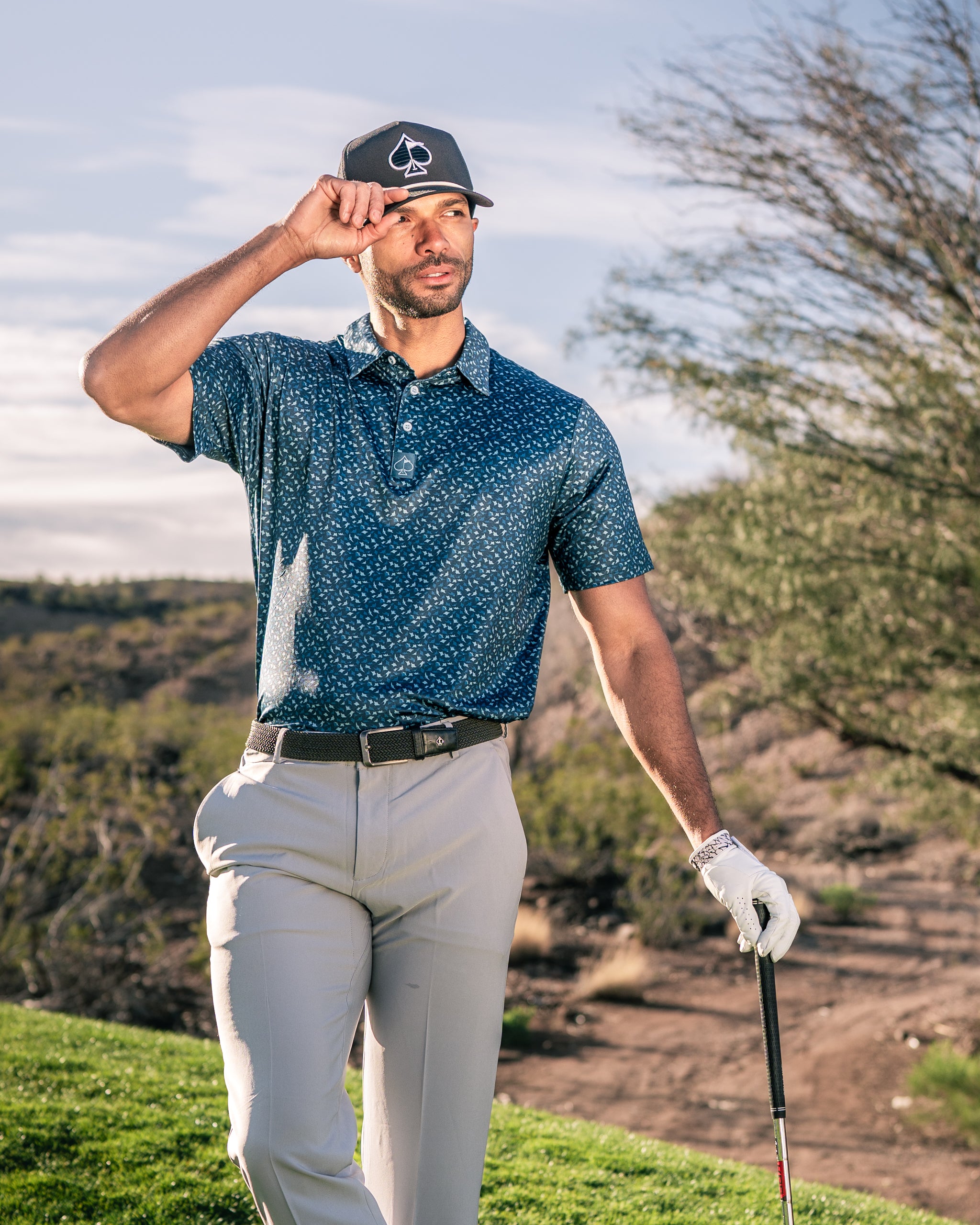 Man wearing a stylish Manta Ray golf polo with a patterned design, holding a golf club on a course.