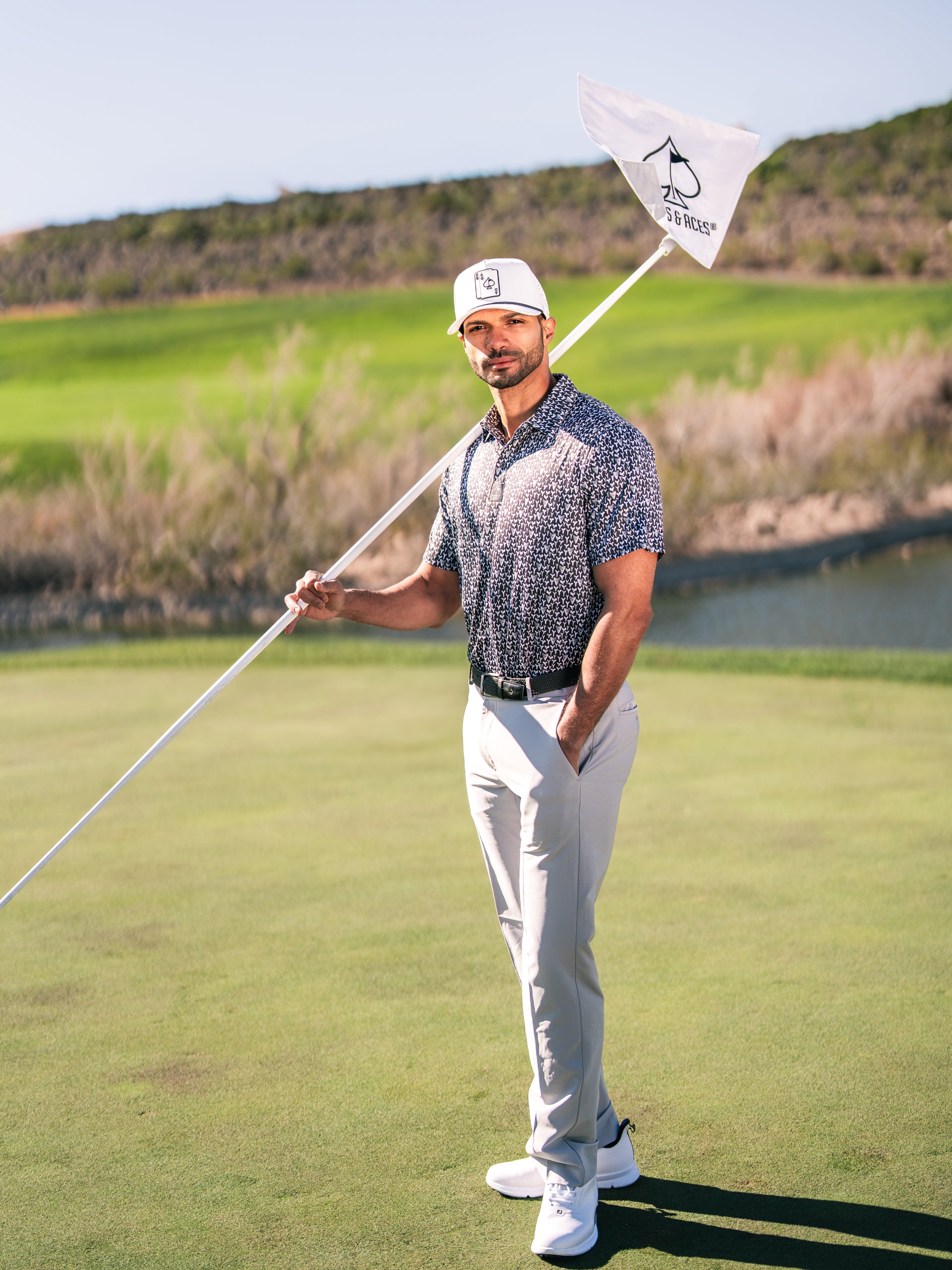 A golfer stands confidently on the green, holding a flag with a shark tooth design, showcasing bold golf apparel.