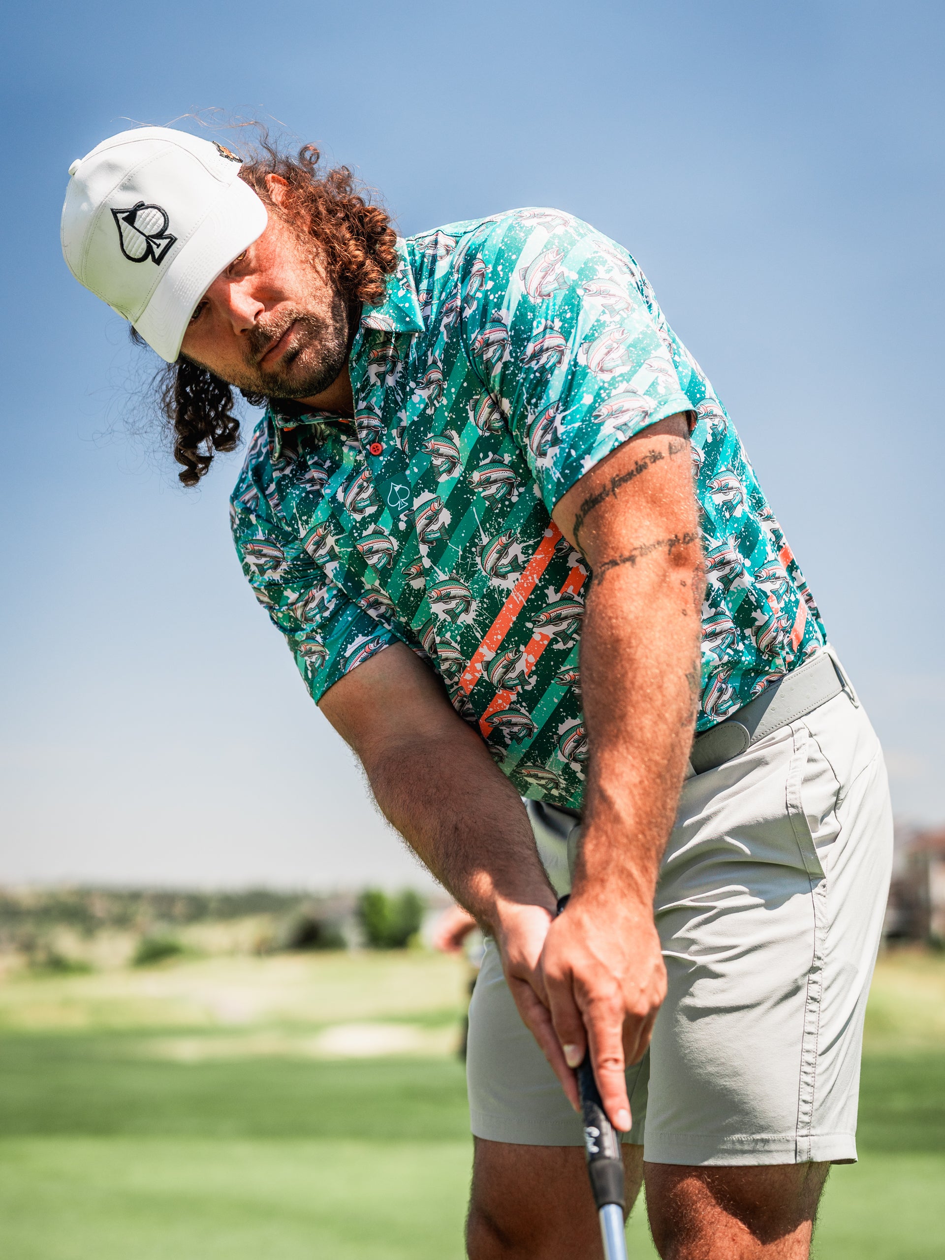 Bold golf shirt featuring a colorful trout splatter design, worn by a golfer preparing to swing on the course.