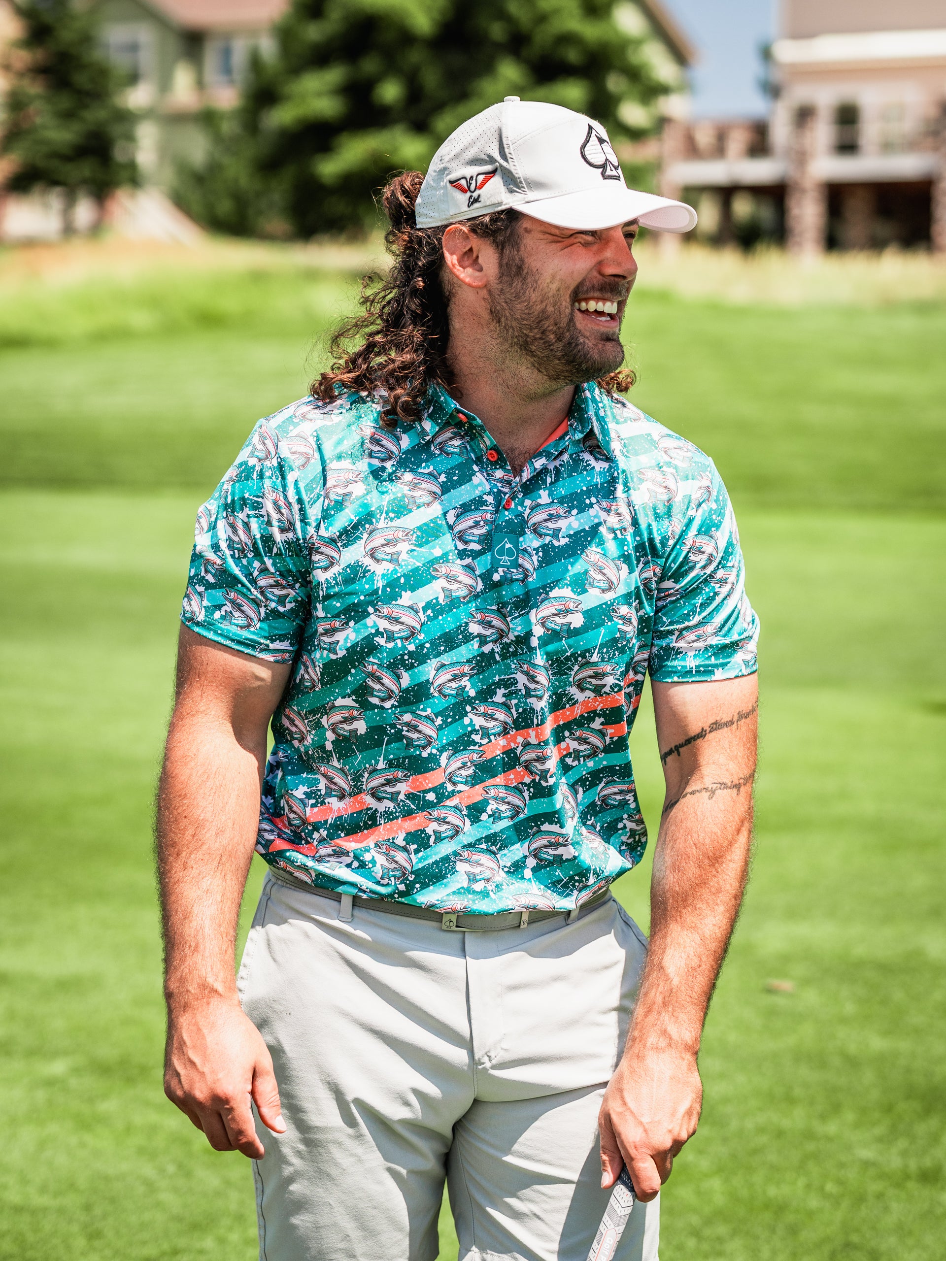 Bold golf shirt featuring a vibrant trout splatter design, worn by a smiling golfer on a sunny course.