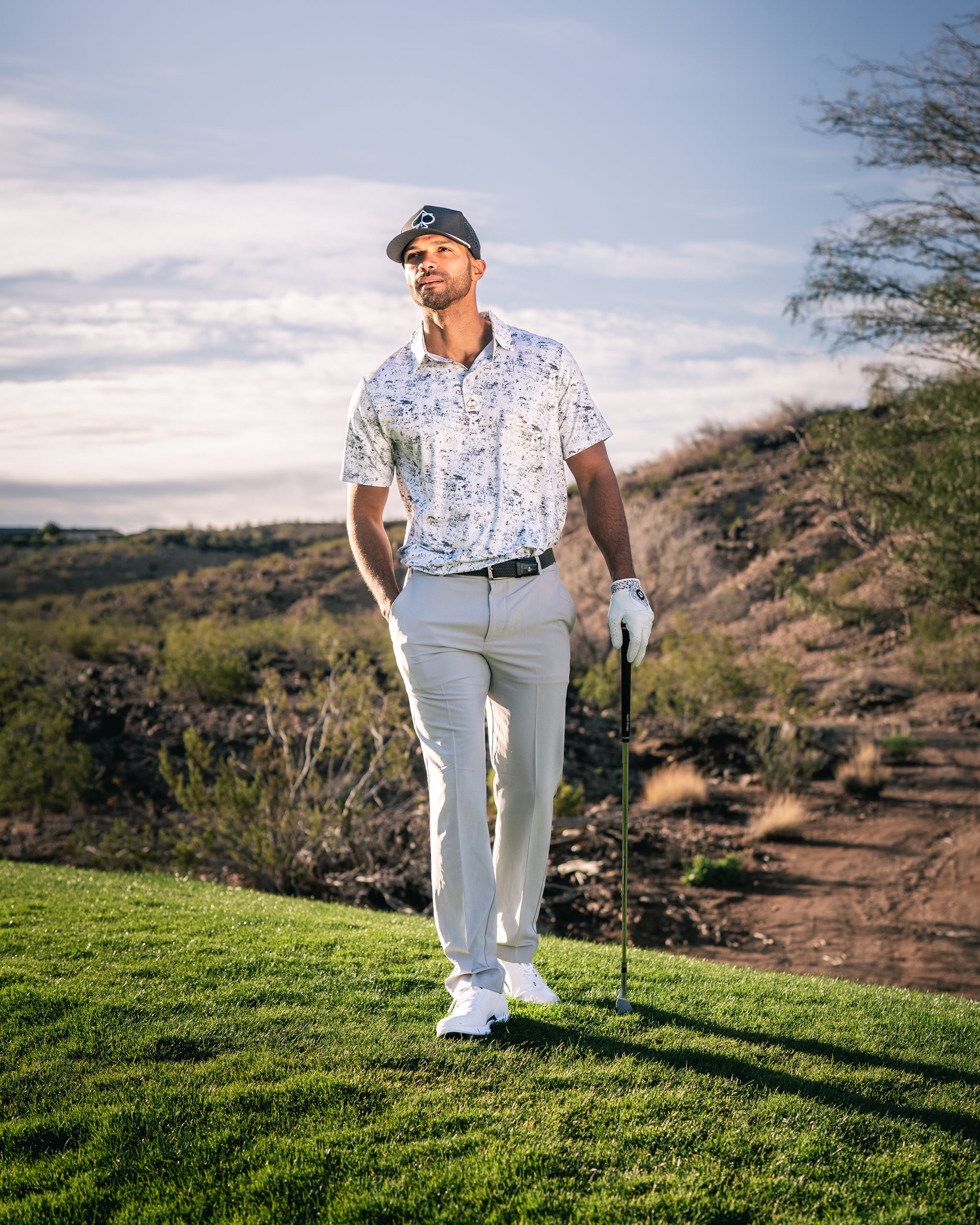 A golfer in a stylish white floral shirt and light pants stands confidently on the course, holding a golf club.
