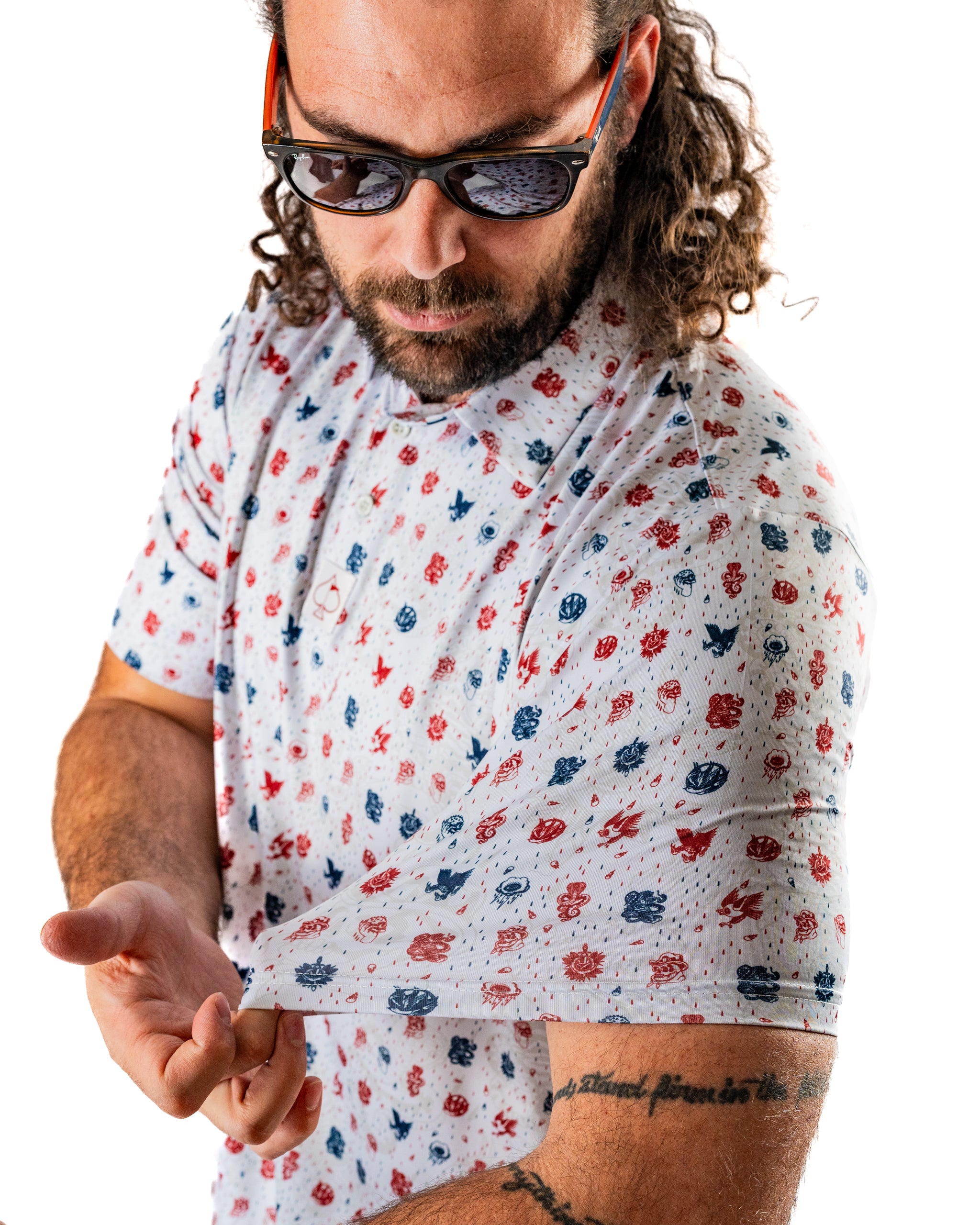 Man showcasing the American Traditional golf shirt with a colorful pattern, wearing sunglasses and displaying a tattoo.