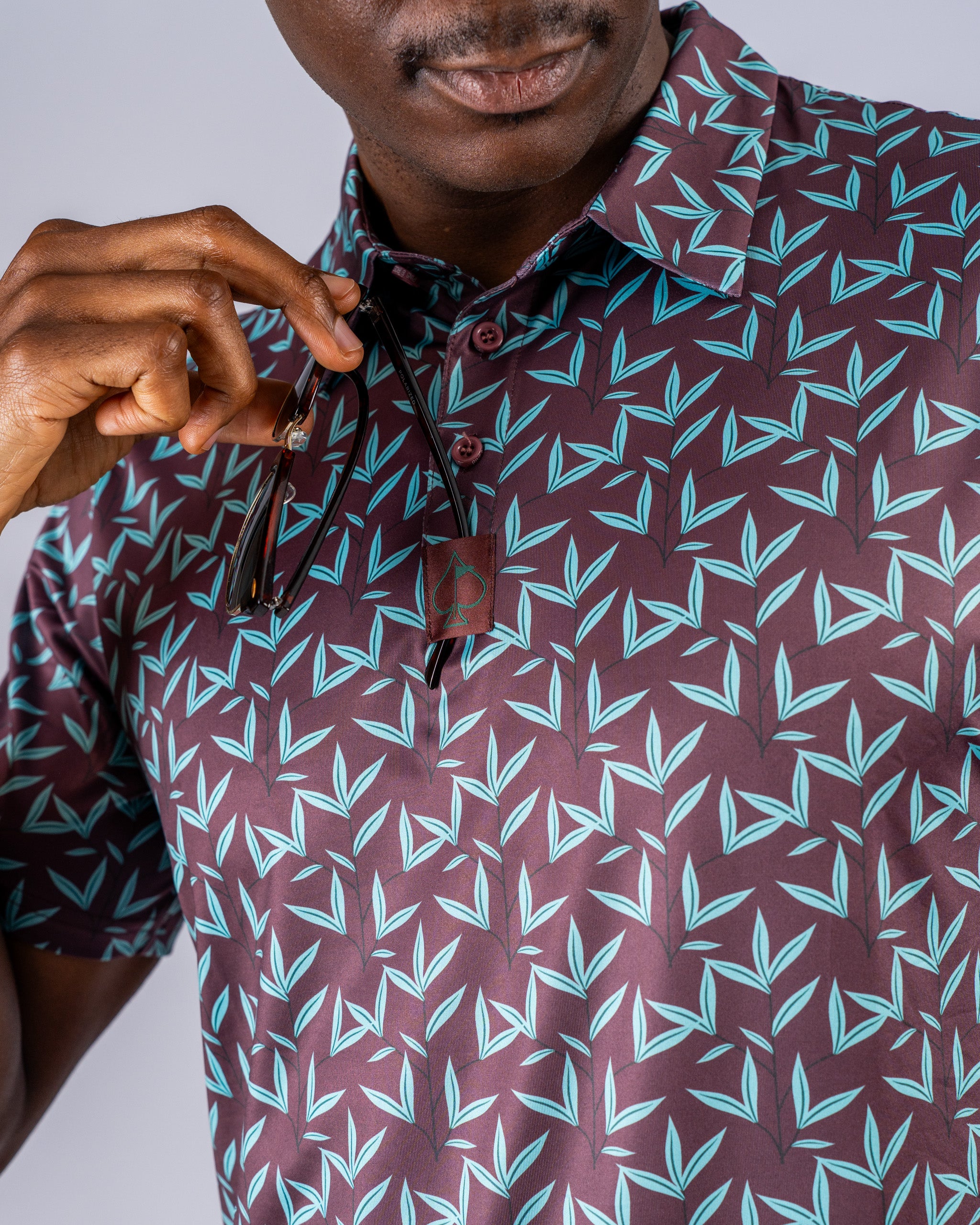 Men's Cocoa Verde golf shirt featuring a bold leaf pattern in teal and maroon, perfect for stylish play on the course.