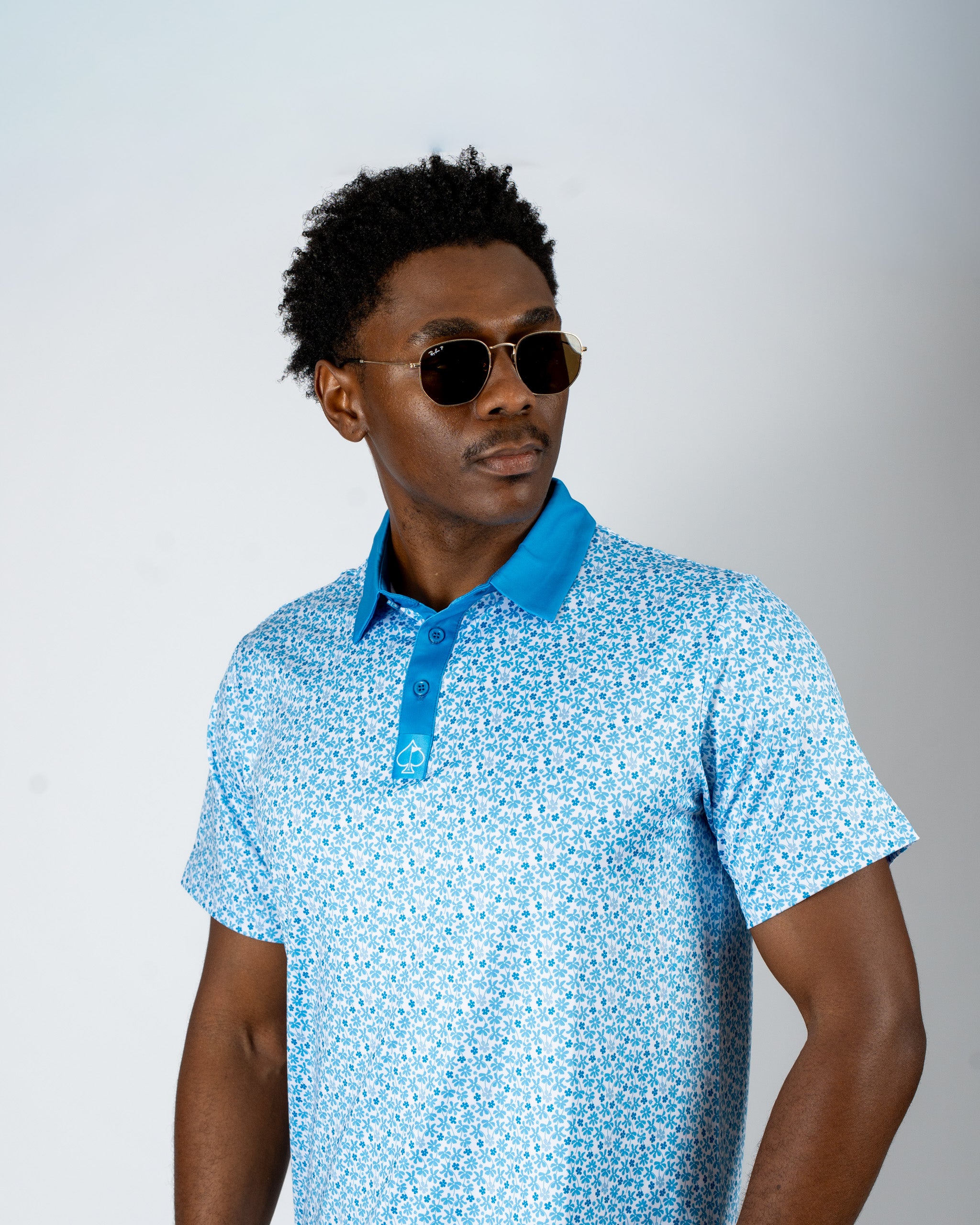 Man wearing a blue floral golf polo shirt with a contrasting collar, styled with sunglasses against a neutral background.
