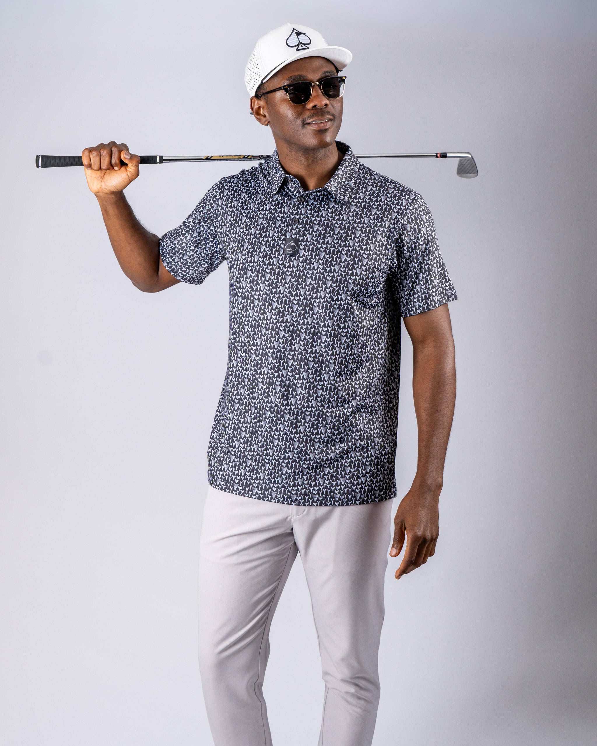Stylish golfer wearing a patterned shirt and sunglasses, holding a golf club, showcasing bold golf apparel.