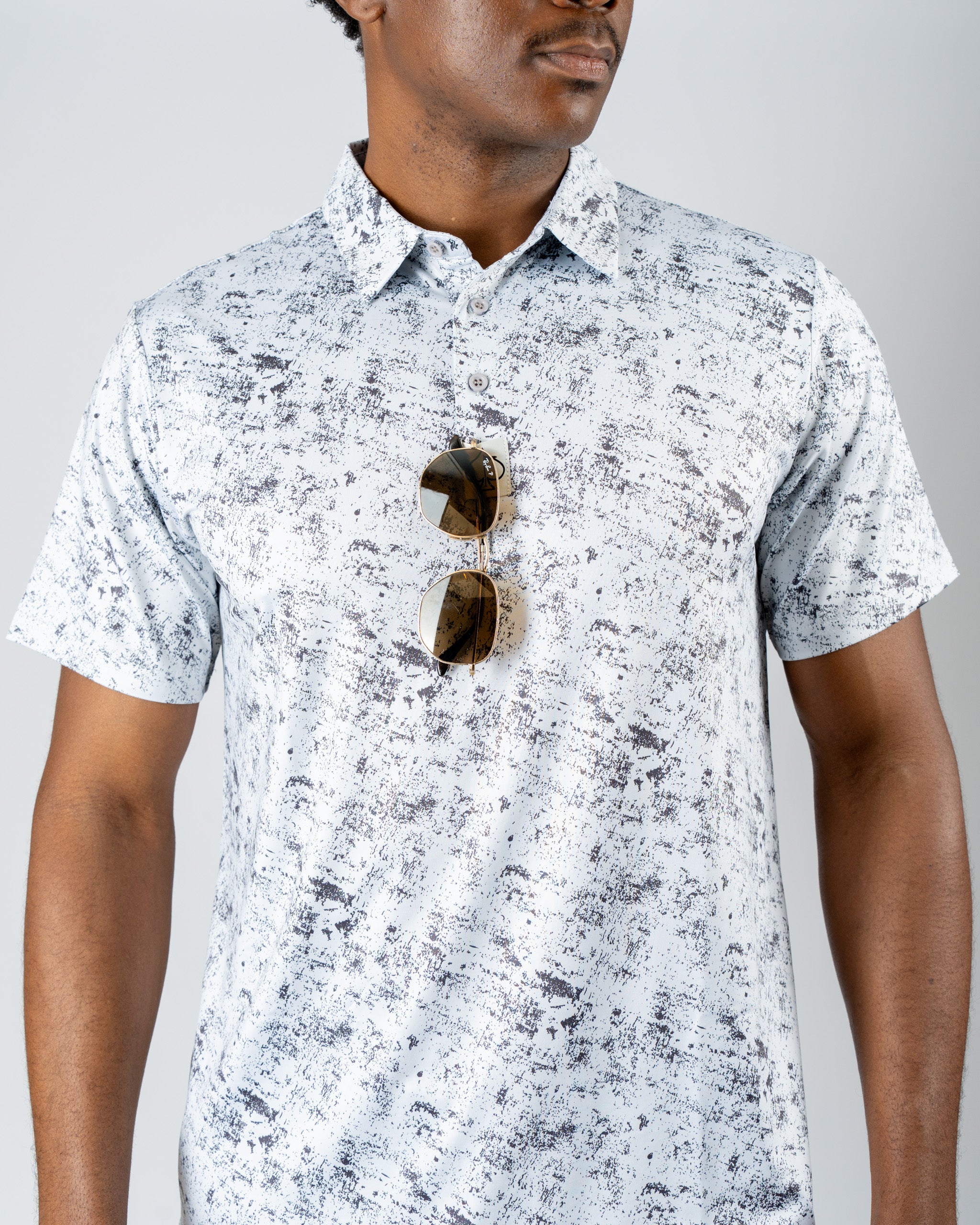 Men's short-sleeve golf shirt in a white and gray abstract pattern, paired with stylish sunglasses.