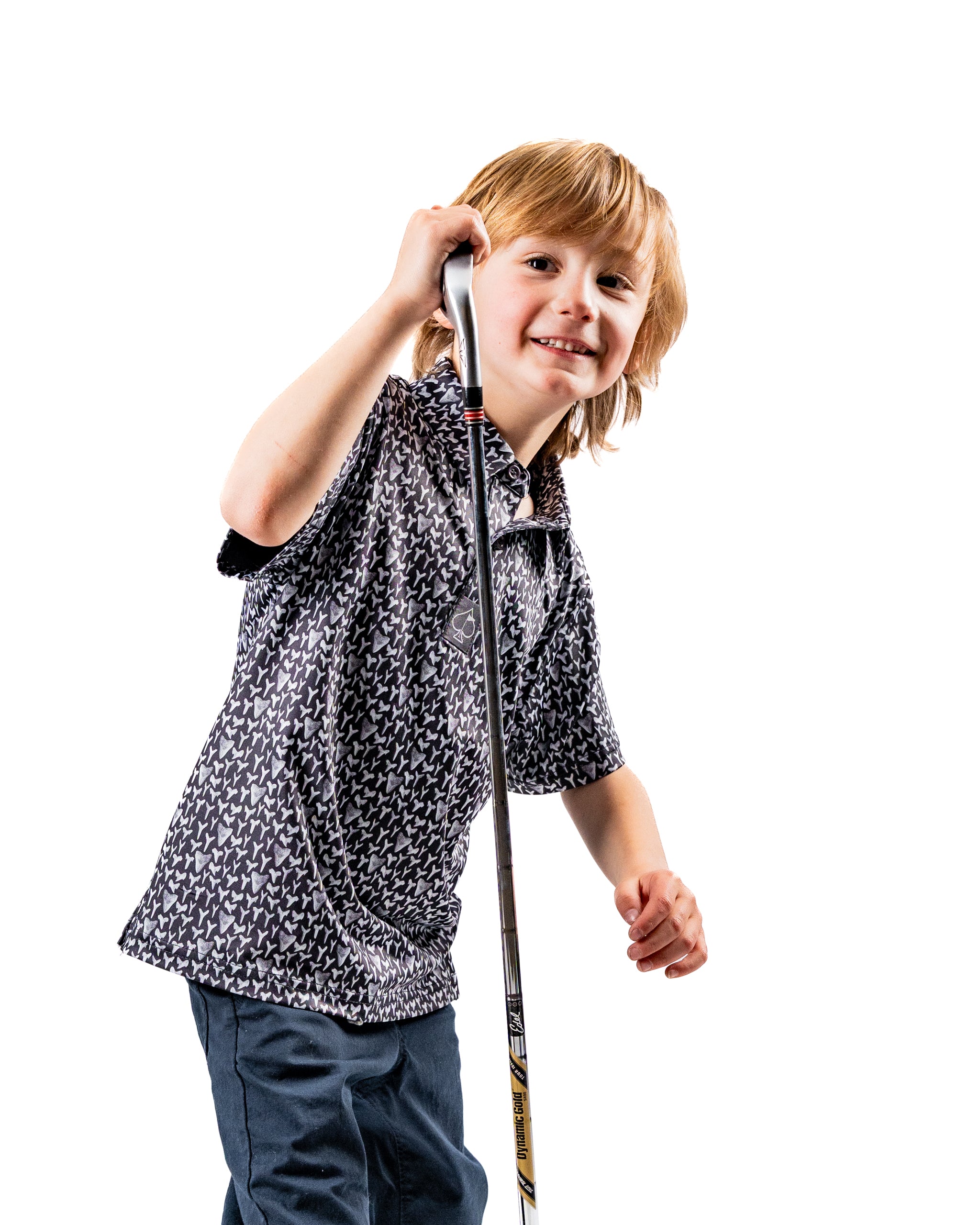 Youth Shark Tooth golf shirt featuring a playful shark tooth pattern, worn by a smiling boy holding a golf club.