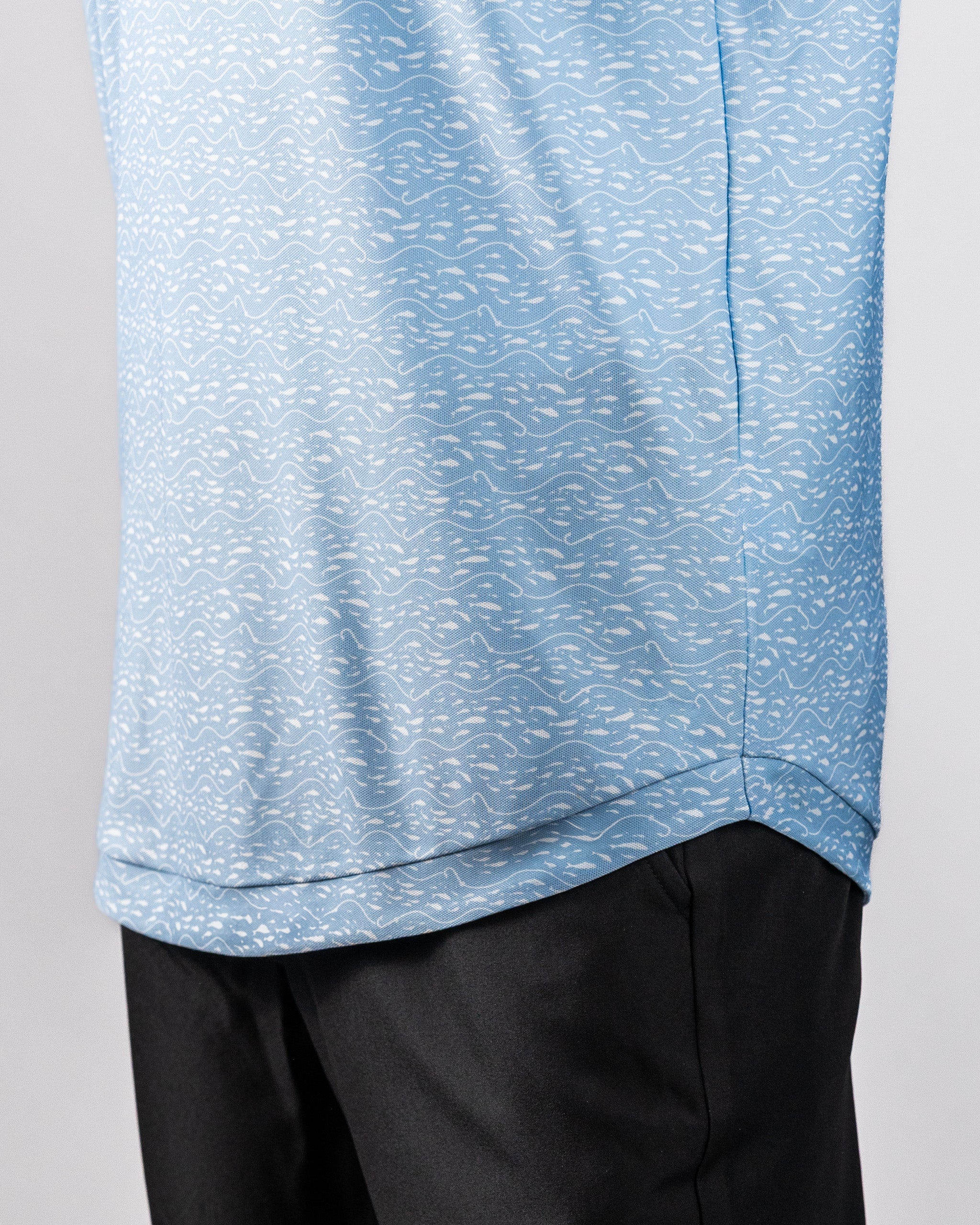 Close-up of a light blue Player Preferred™ Polo shirt with a subtle wave pattern, worn over black pants.