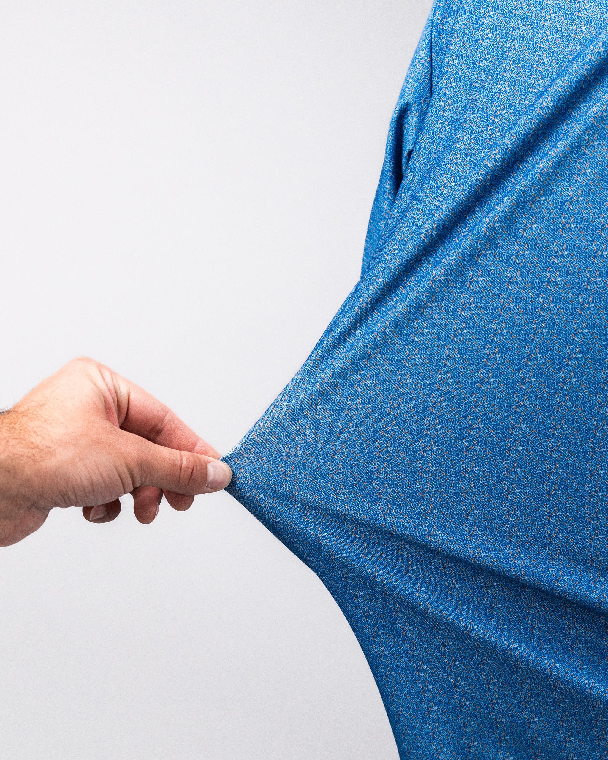 Close-up of a hand stretching a blue Player Preferred™ Polo - Cosmic Swirl fabric, showcasing its vibrant, textured pattern.