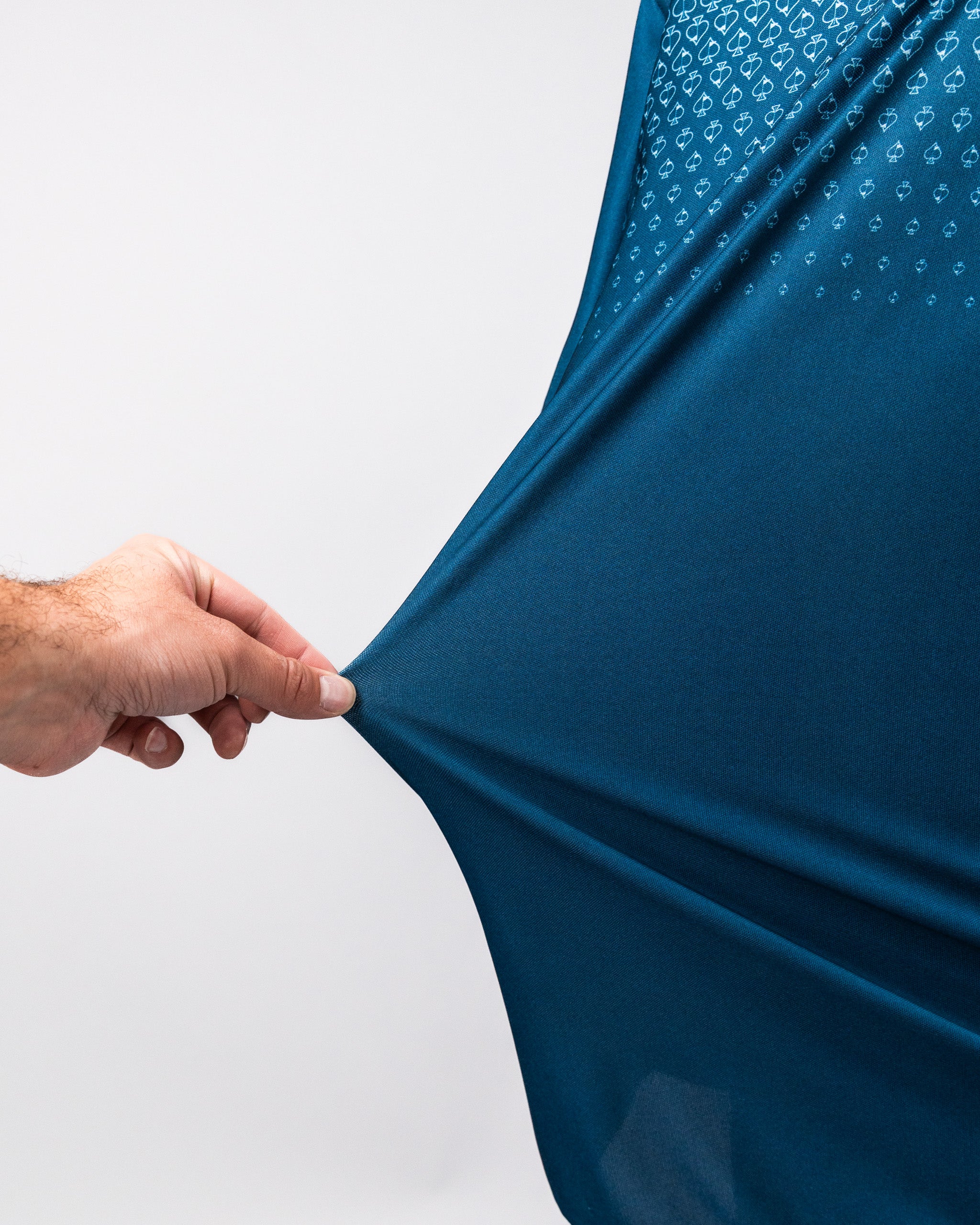 Close-up of a hand stretching a navy Player Preferred™ Polo shirt with Spade Fade pattern, showing the fabric's stretch and texture.