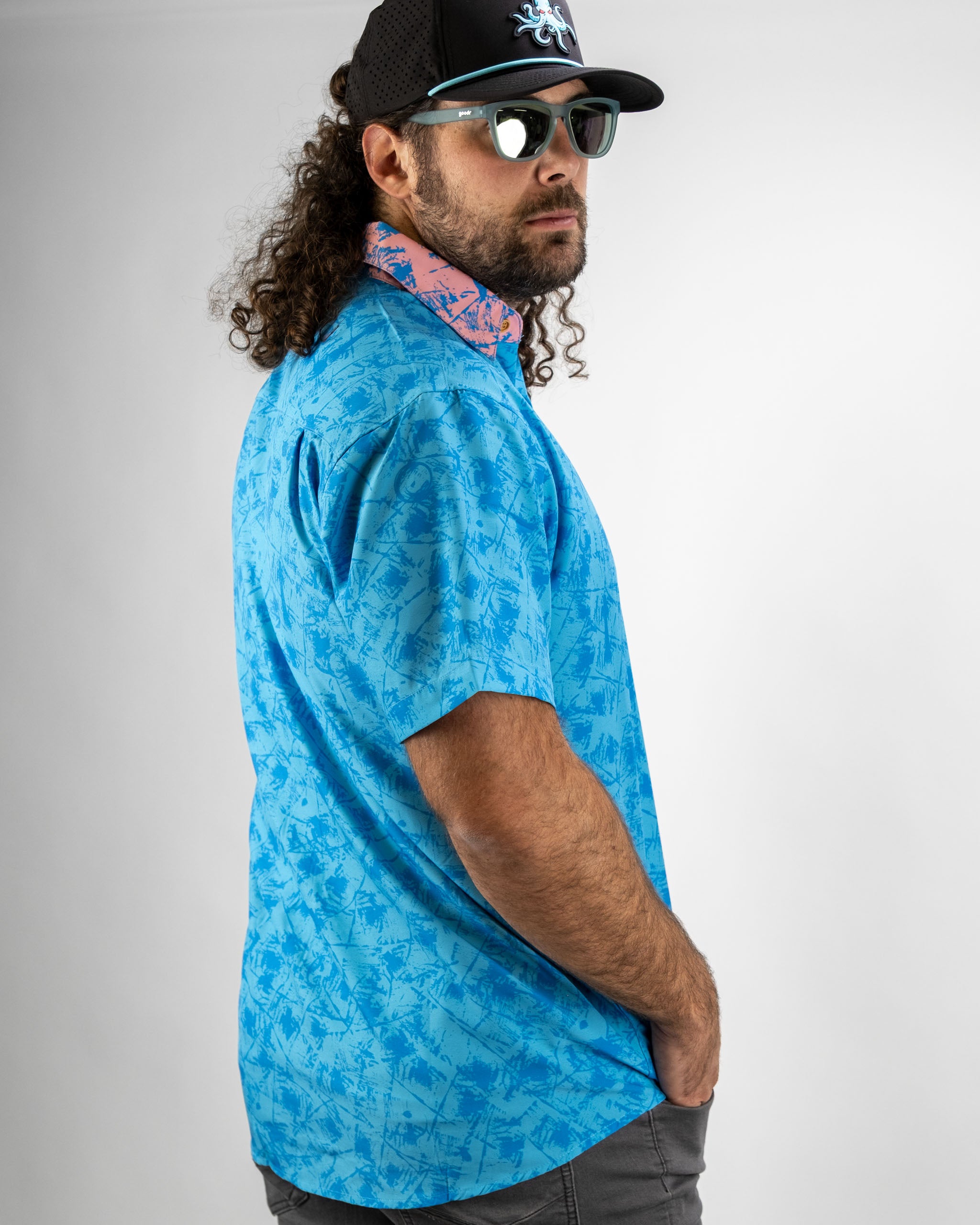 Man wearing a blue short-sleeve shirt with a pastel pattern, complemented by a pink patterned collar and sunglasses.