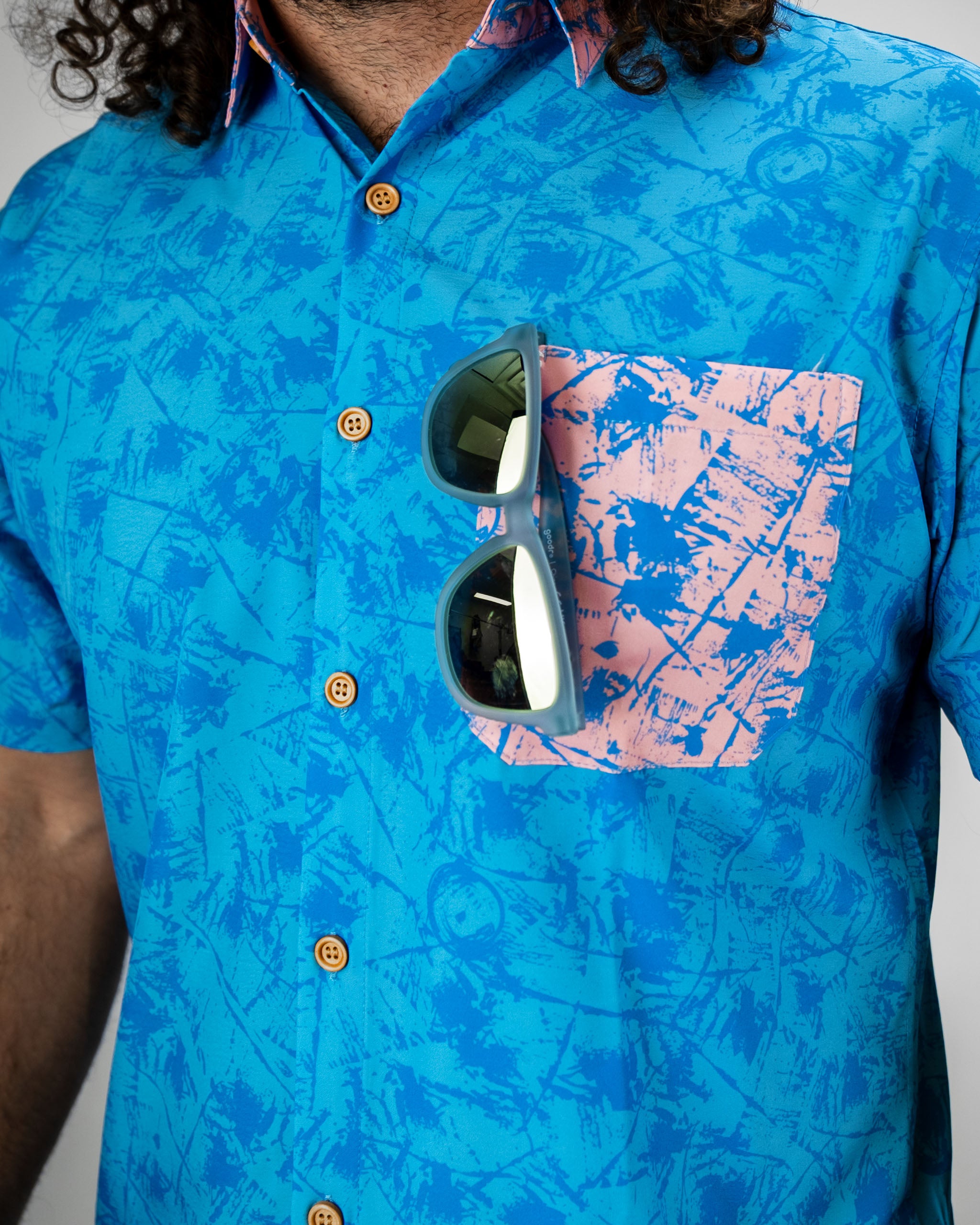 Bright blue button-up shirt with a pink patterned pocket, featuring a model wearing sunglasses. Perfect for stylish golf outings.