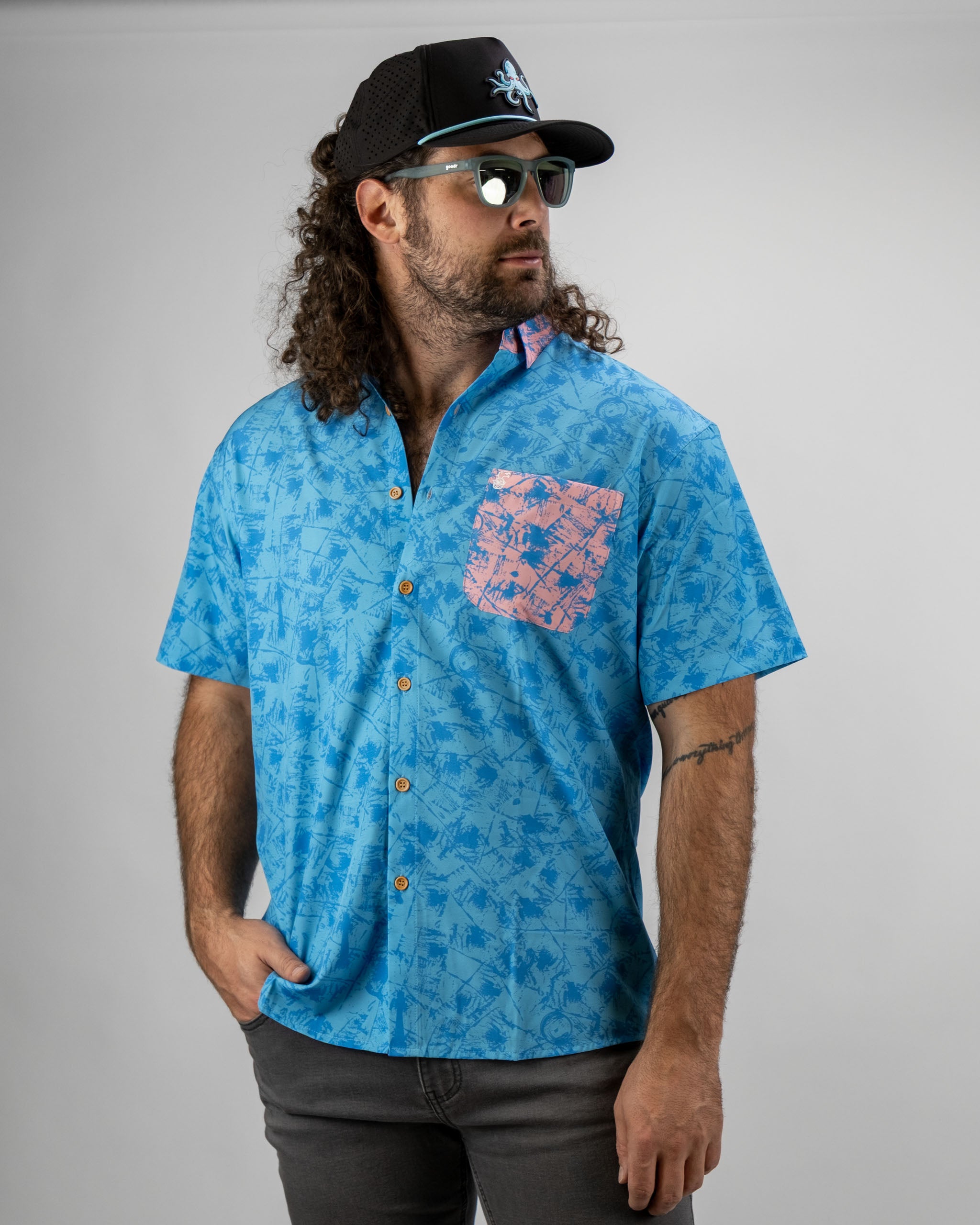 Men's blue short-sleeve shirt featuring a pink pocket and tropical print, perfect for stylish golf outings.
