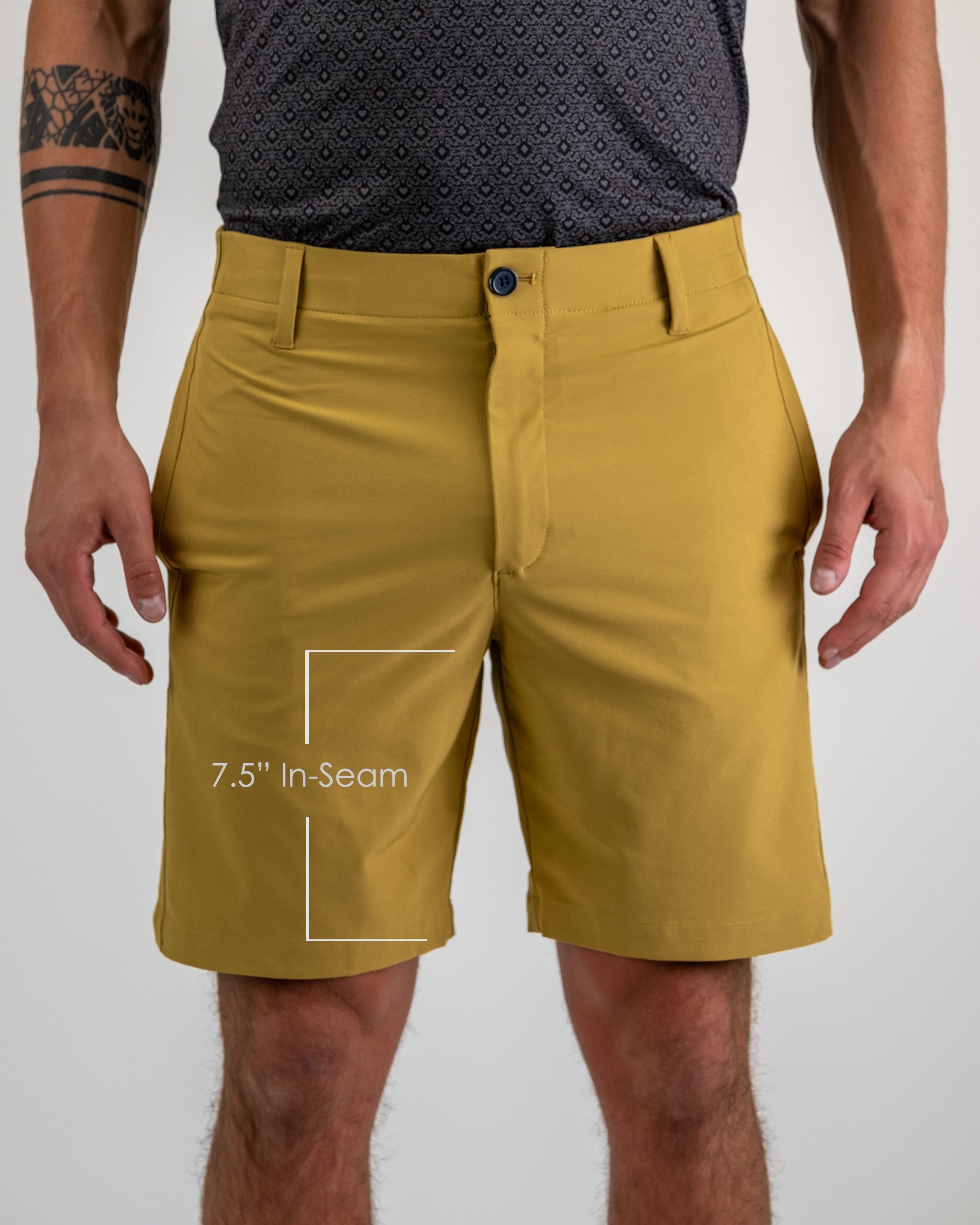 Close-up of mustard yellow golf shorts with a 7.5-inch inseam, worn by a golfer with tattoos, paired with a patterned blac...