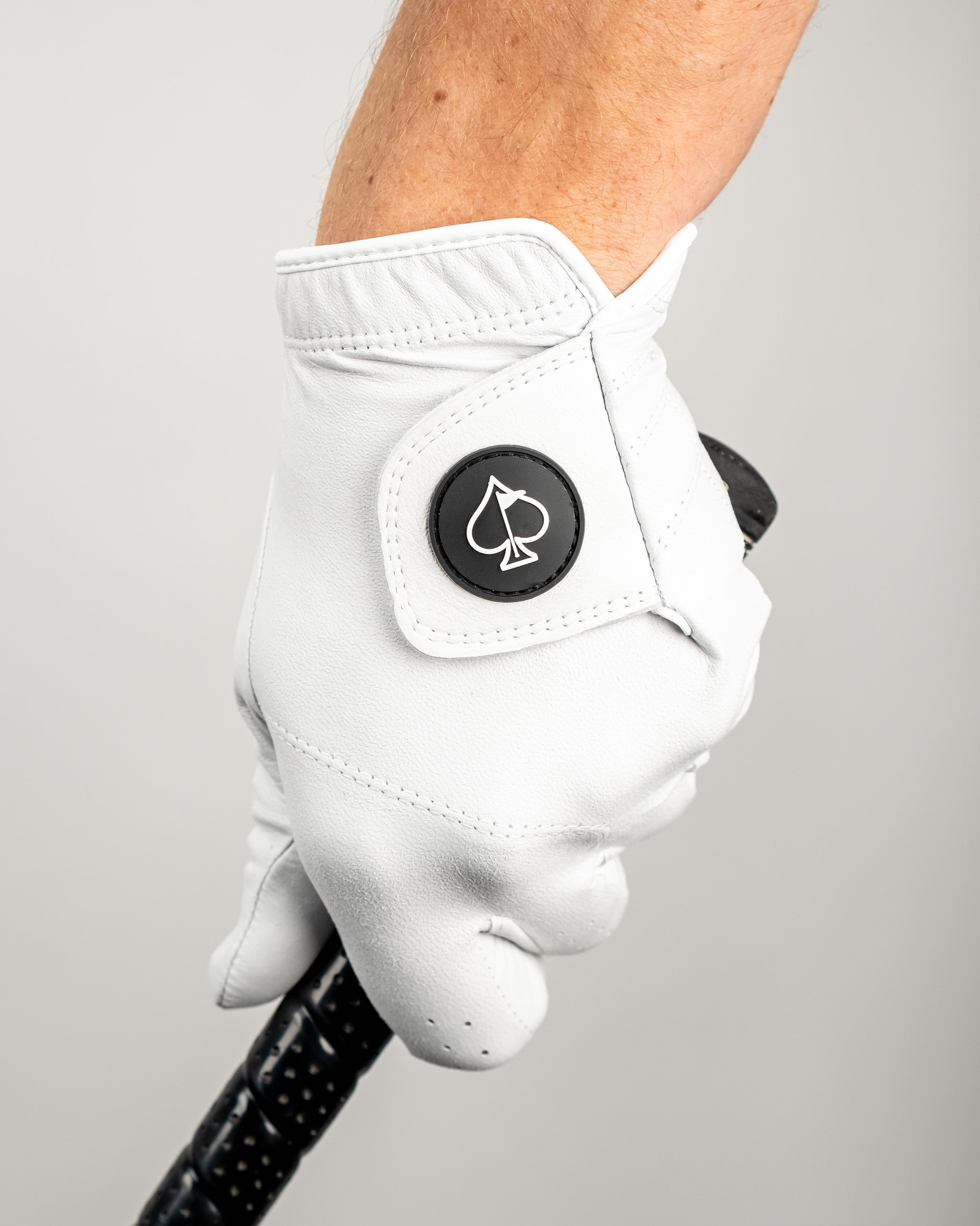 White golf glove with black spade logo patch, designed for bold, standout golf style and accessories.