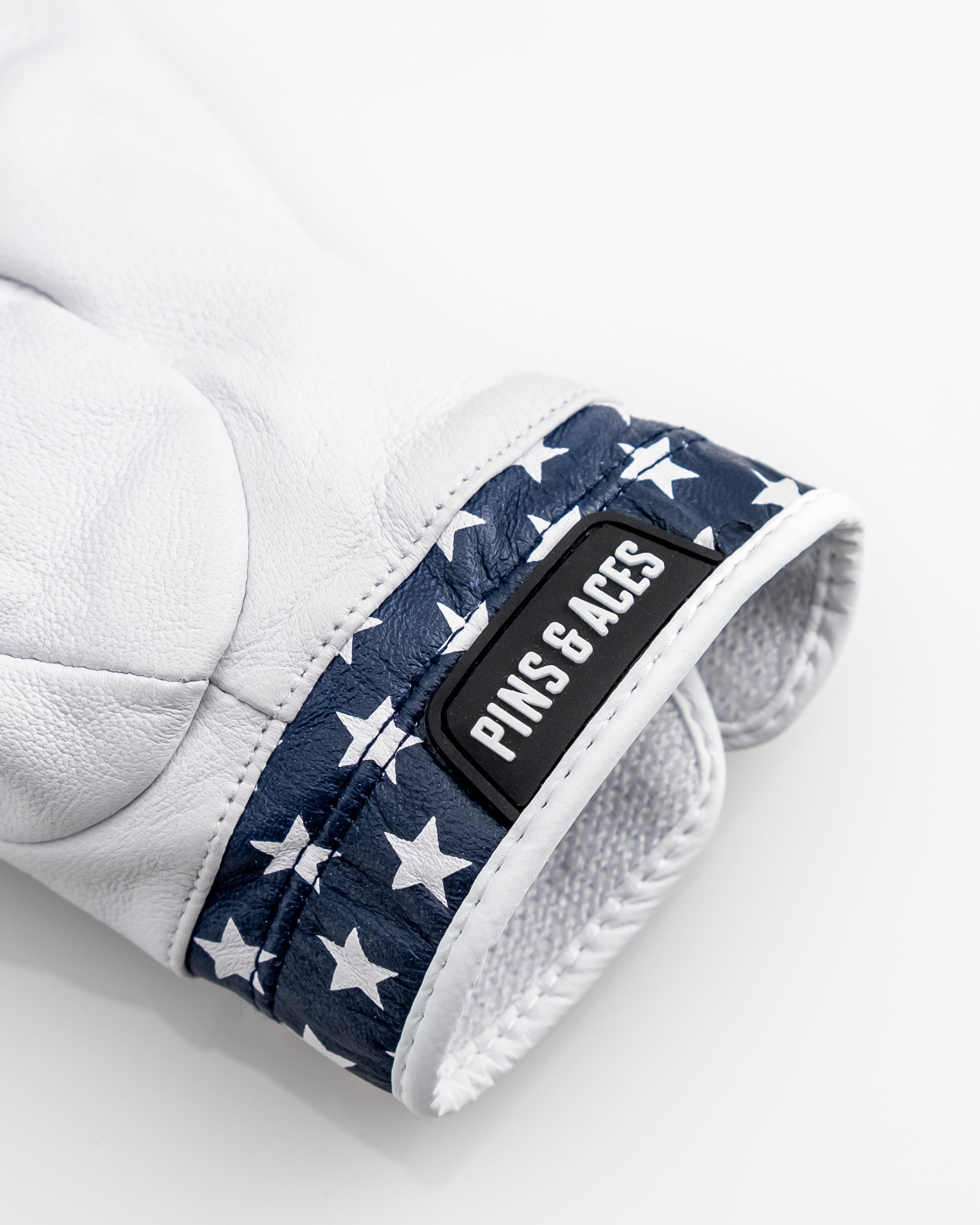 Close-up of a white golf glove with a navy blue star pattern, labeled "PINS & ACES" for bold, unique golf style.