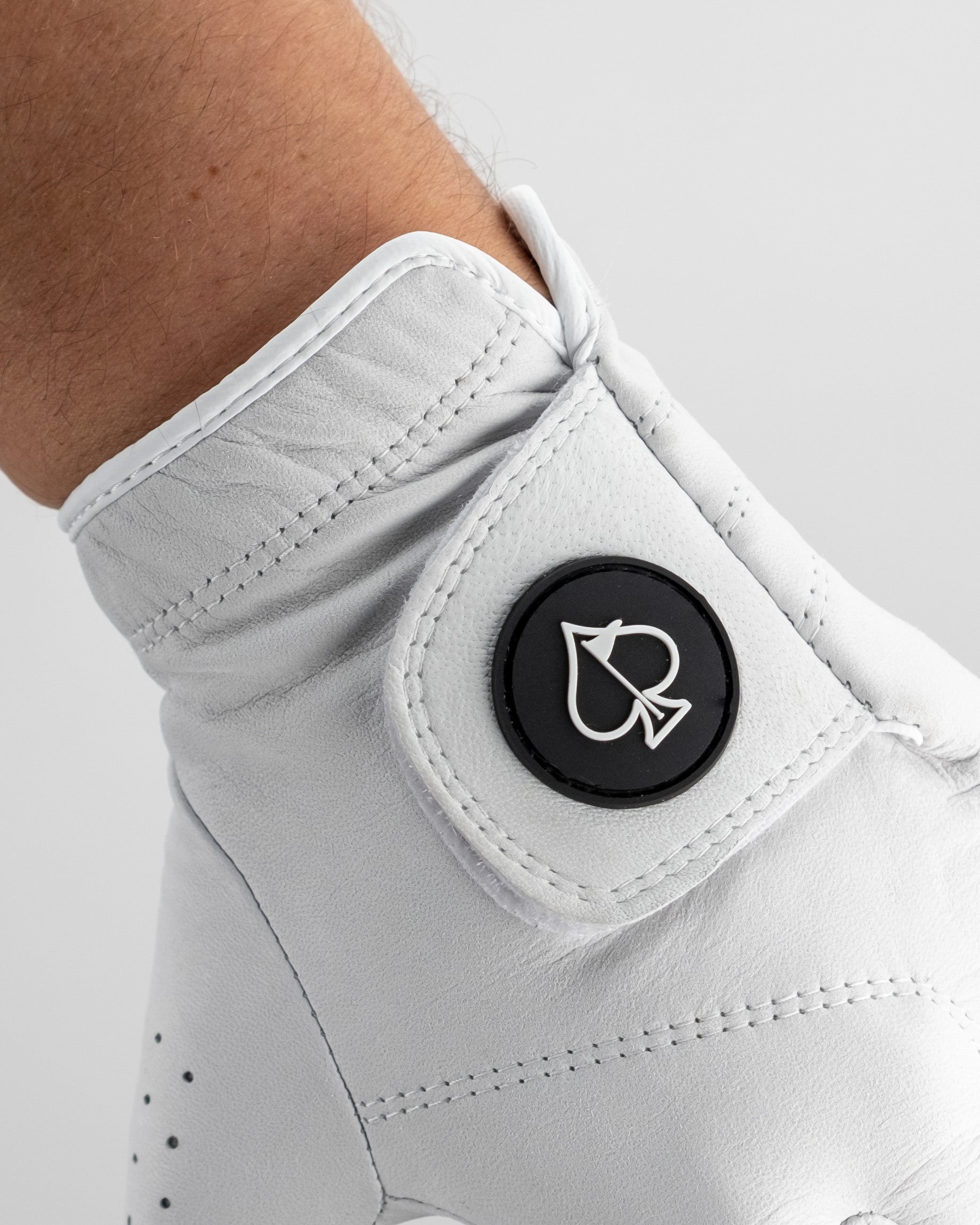 Close-up of a white golf shoe with a black circular logo featuring a stylized golf club and ball, highlighting bold, uniqu...