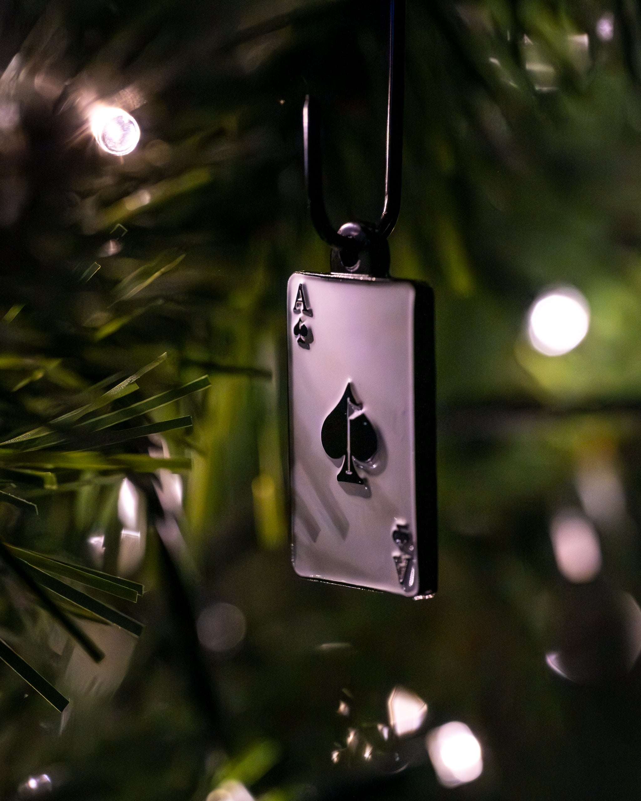 Ace of Spades card ornament hanging on a Christmas tree, illuminated by soft glowing lights.
