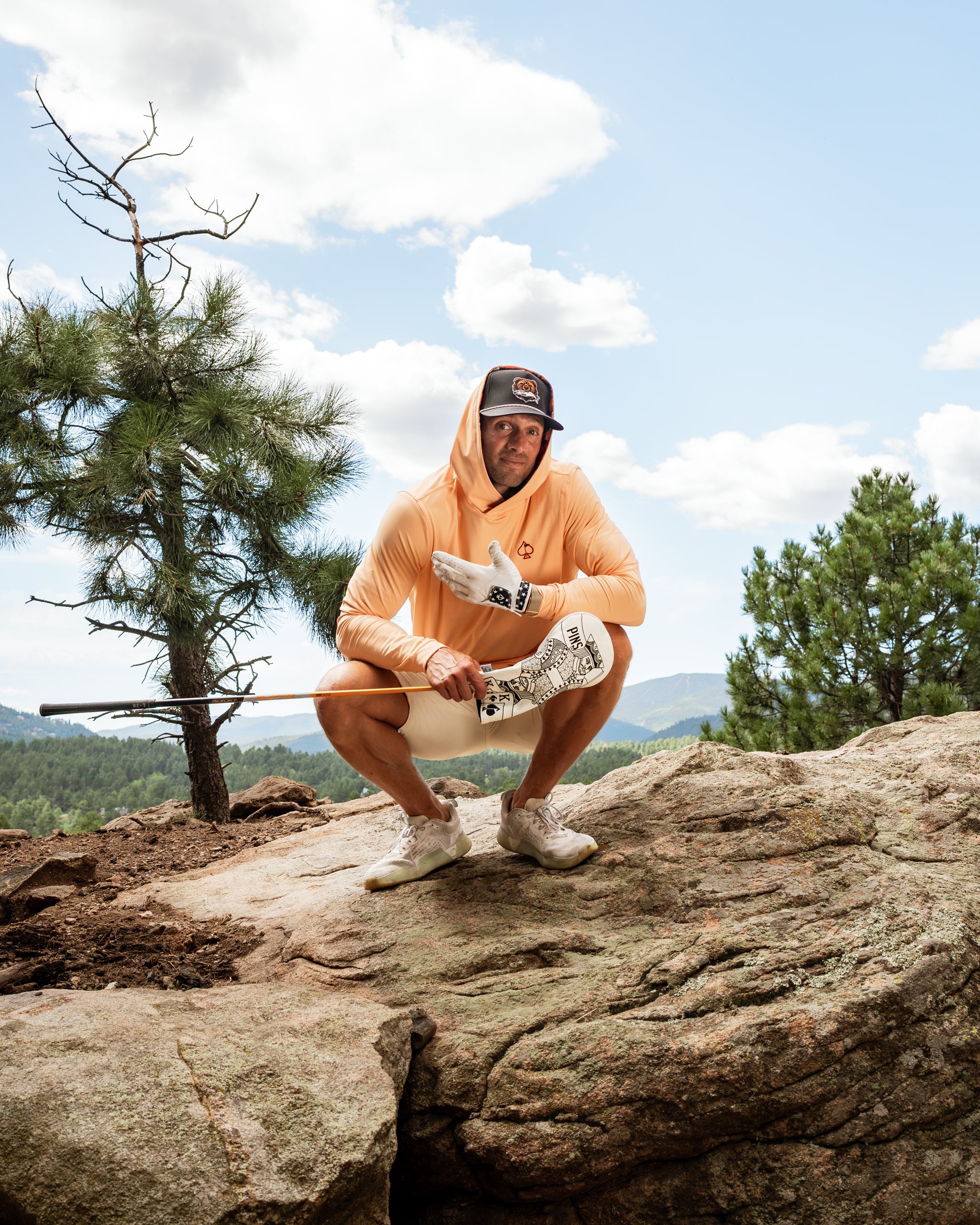 Performance golf hoodie in autumn leaves color, worn by a golfer posing on a rocky terrain with a golf club.