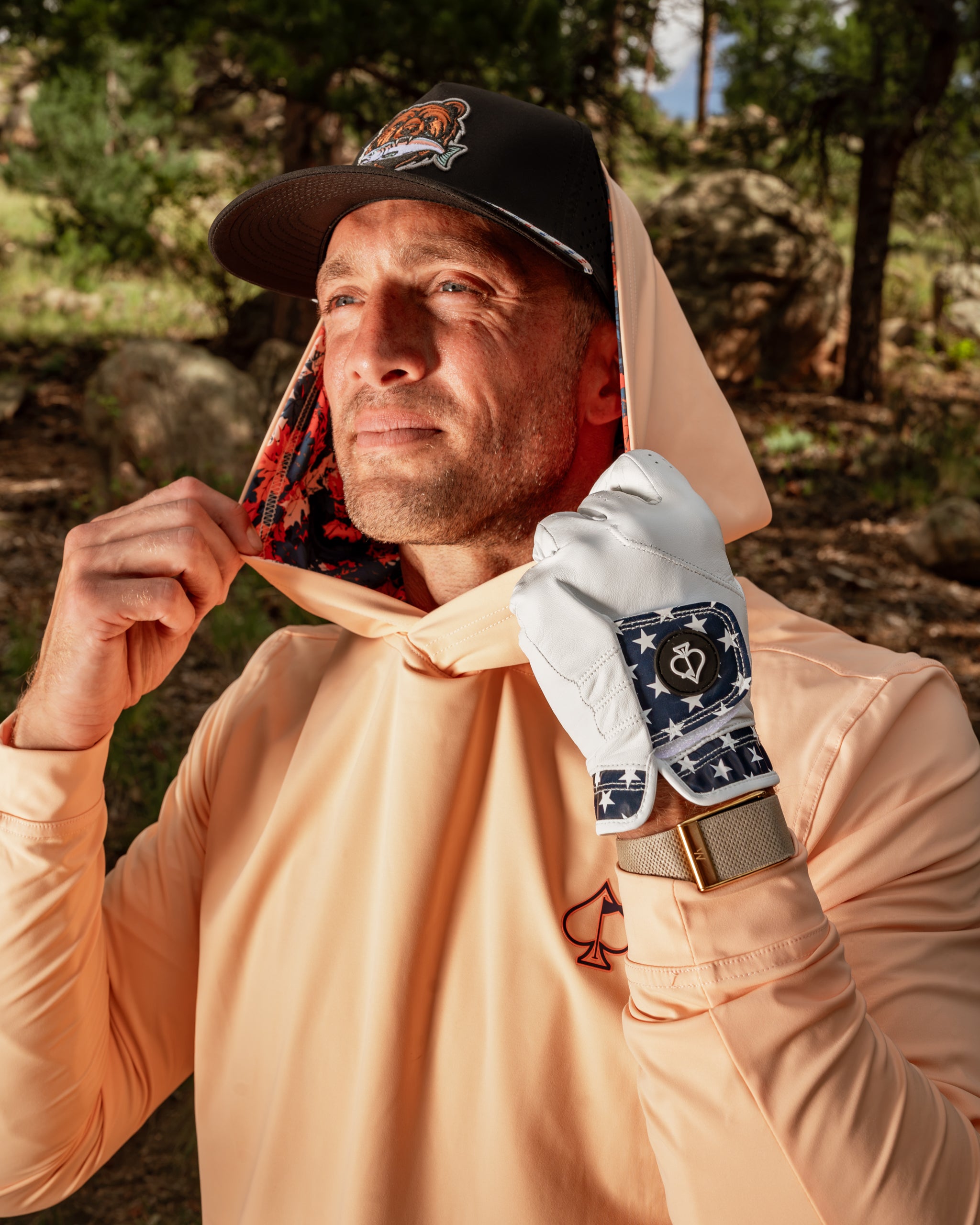 Man wearing a performance golf hoodie in autumn leaves color, adjusting the hood in a natural outdoor setting.