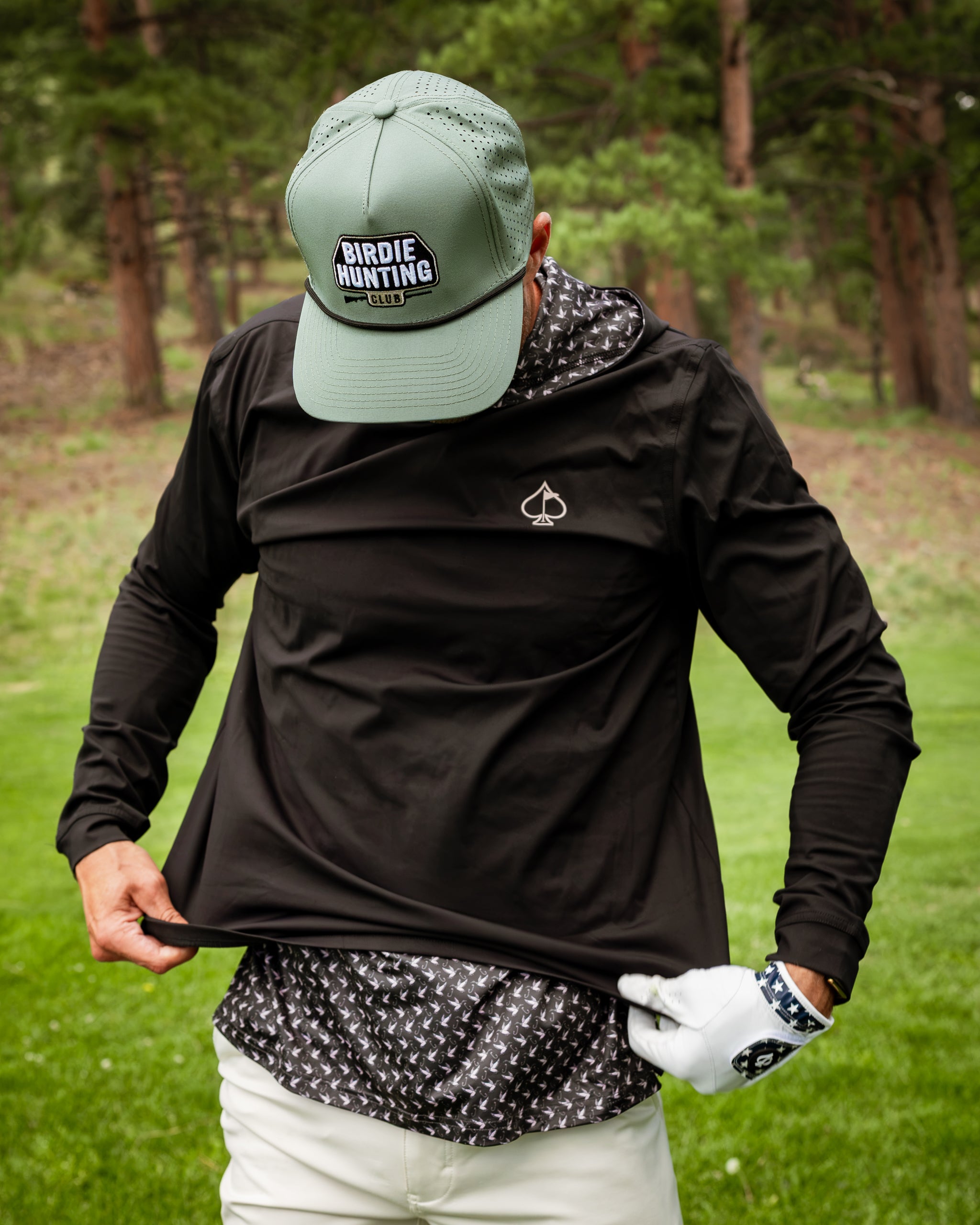 Performance Golf Hoodie in black, featuring a stylish design, worn by a golfer adjusting the hem on the course.