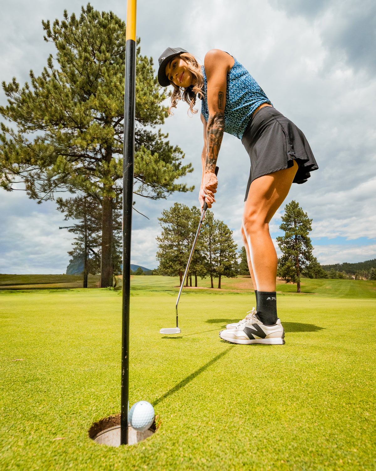 Woman in a navy and white golf outfit prepares to putt on a lush green course with a flag stick in the background.