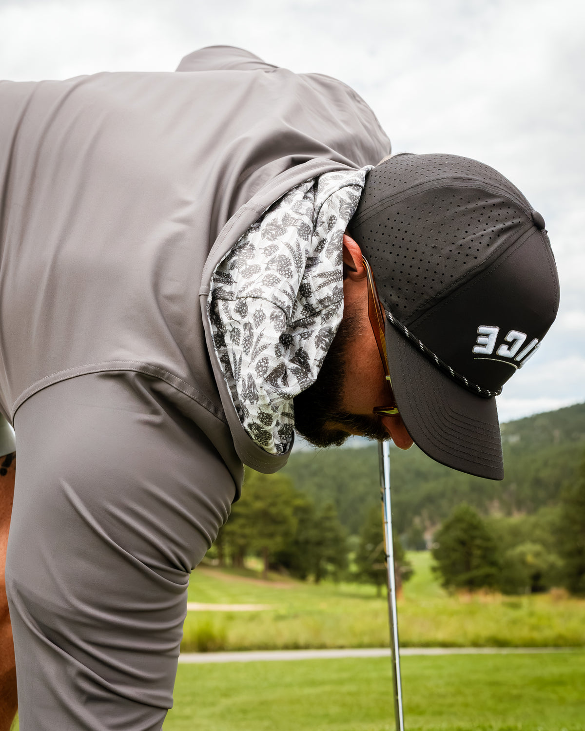 Performance golf hoodie in gray with a patterned hood, worn by a golfer focusing on their swing on a lush course.