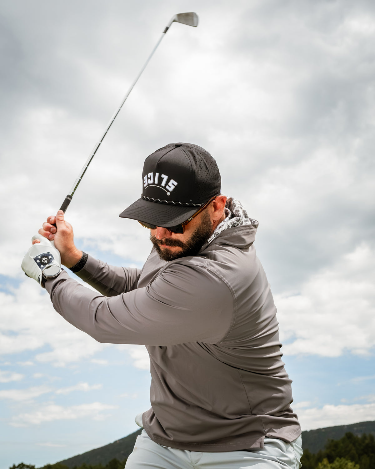 Man swinging a golf club while wearing a Performance Golf Hoodie in Hops & Barely, showcasing a stylish and functional design.