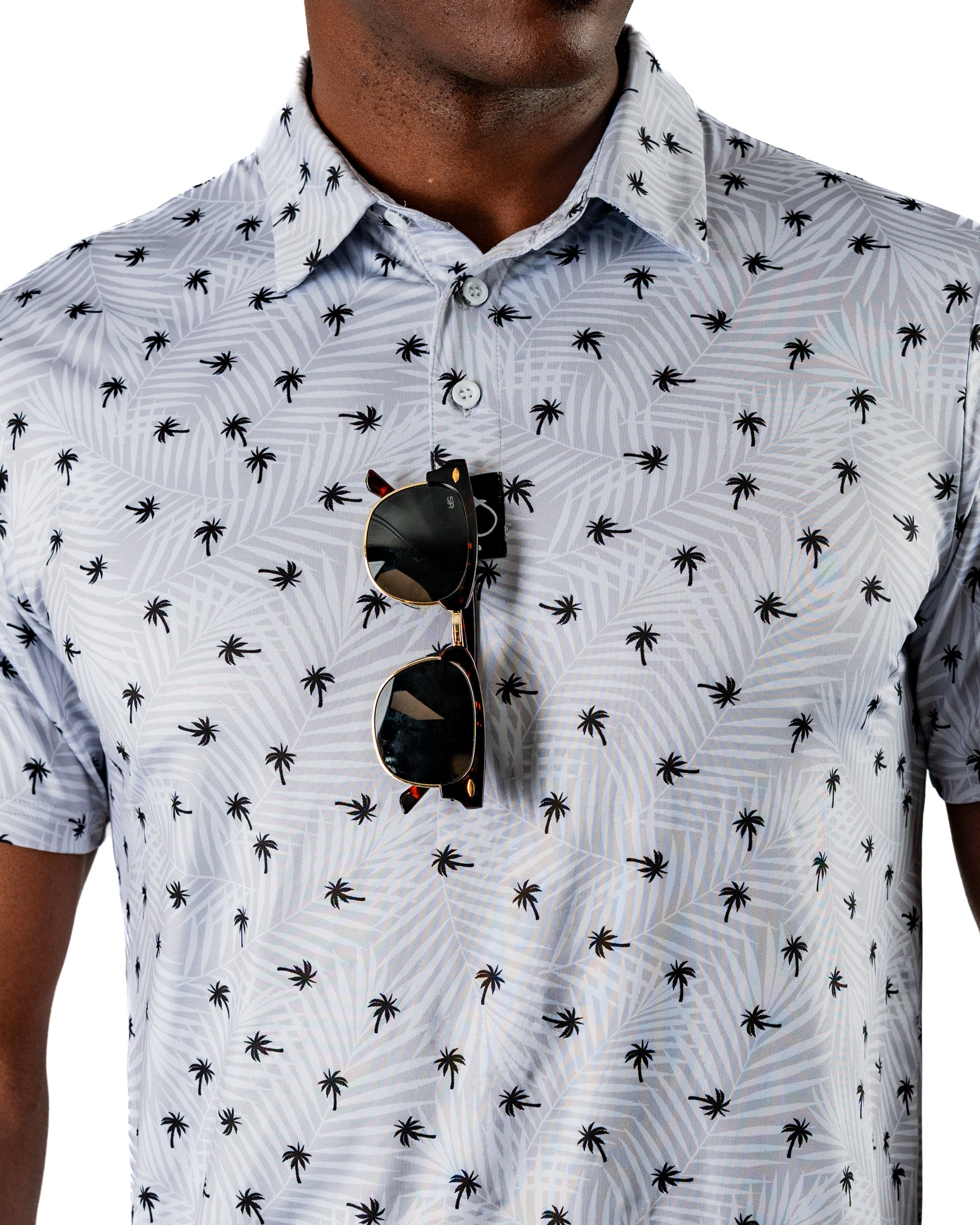 Men's short-sleeve shirt featuring a palm tree pattern, paired with sunglasses for a stylish, tropical golf look.