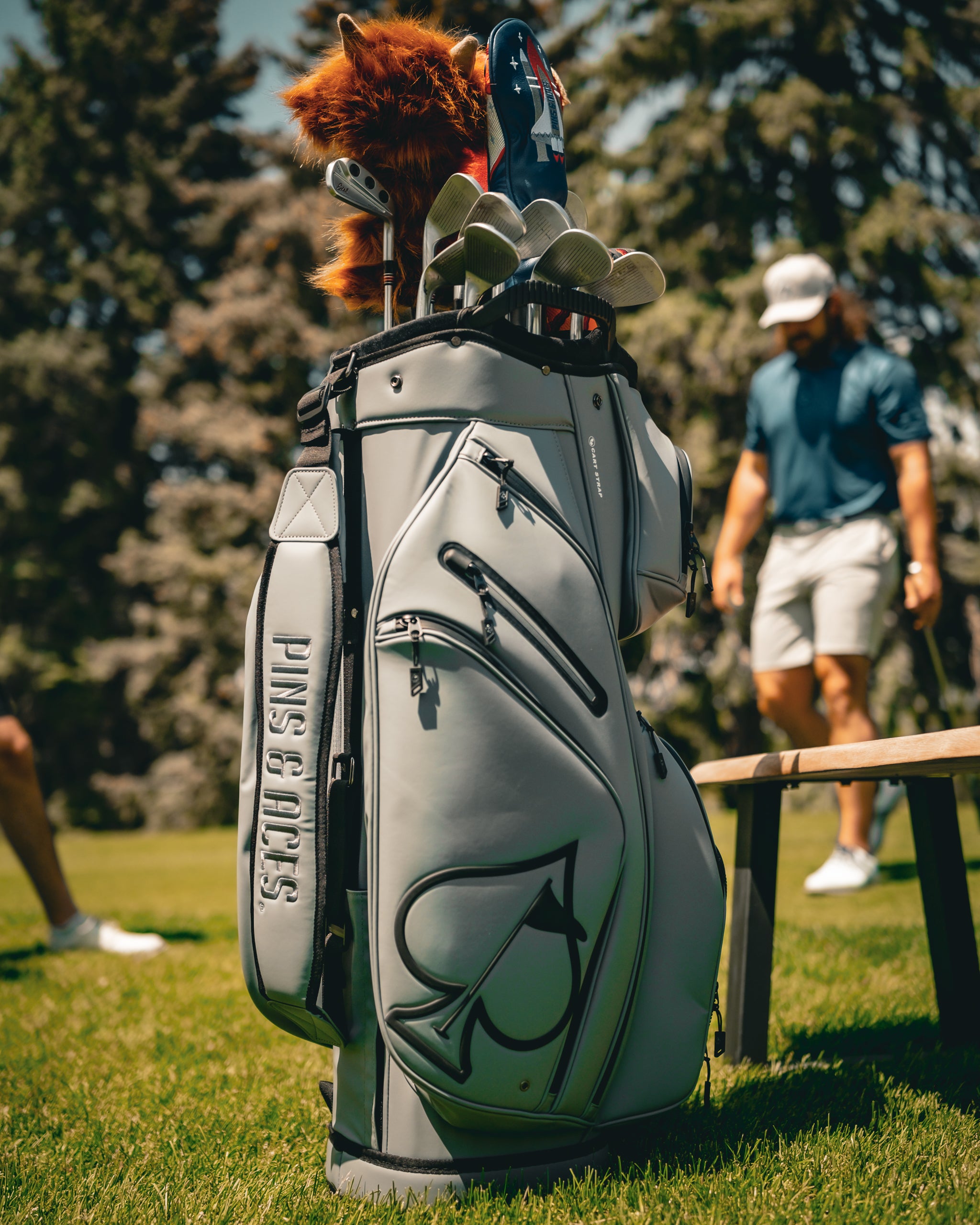 Player Preferred Cart Bag in Flat Ash color, featuring multiple pockets and clubs, set against a golf course backdrop.