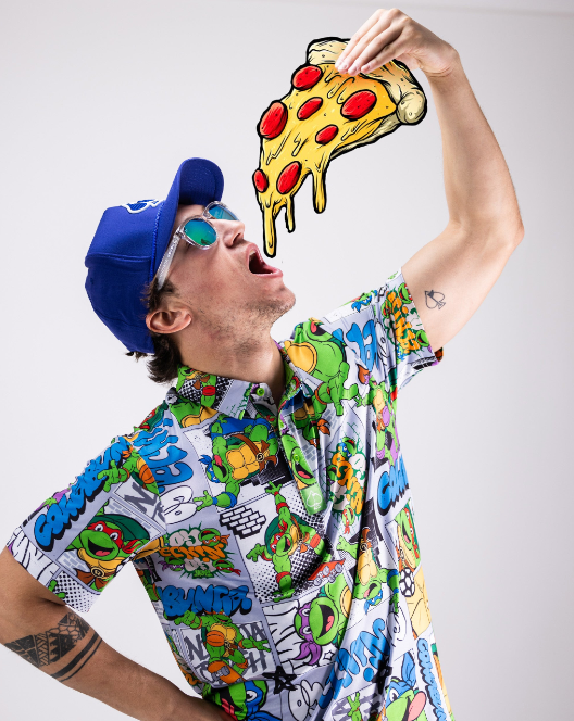 A person wearing a colorful TMNT comic strip shirt poses with a cartoon pizza slice, showcasing a fun, playful style.