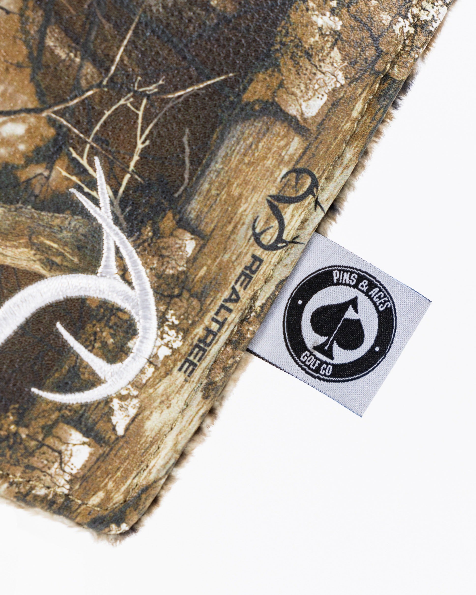 Realtree blade cover featuring a camo design and Pins & Aces logo, perfect for golfers seeking unique accessories.
