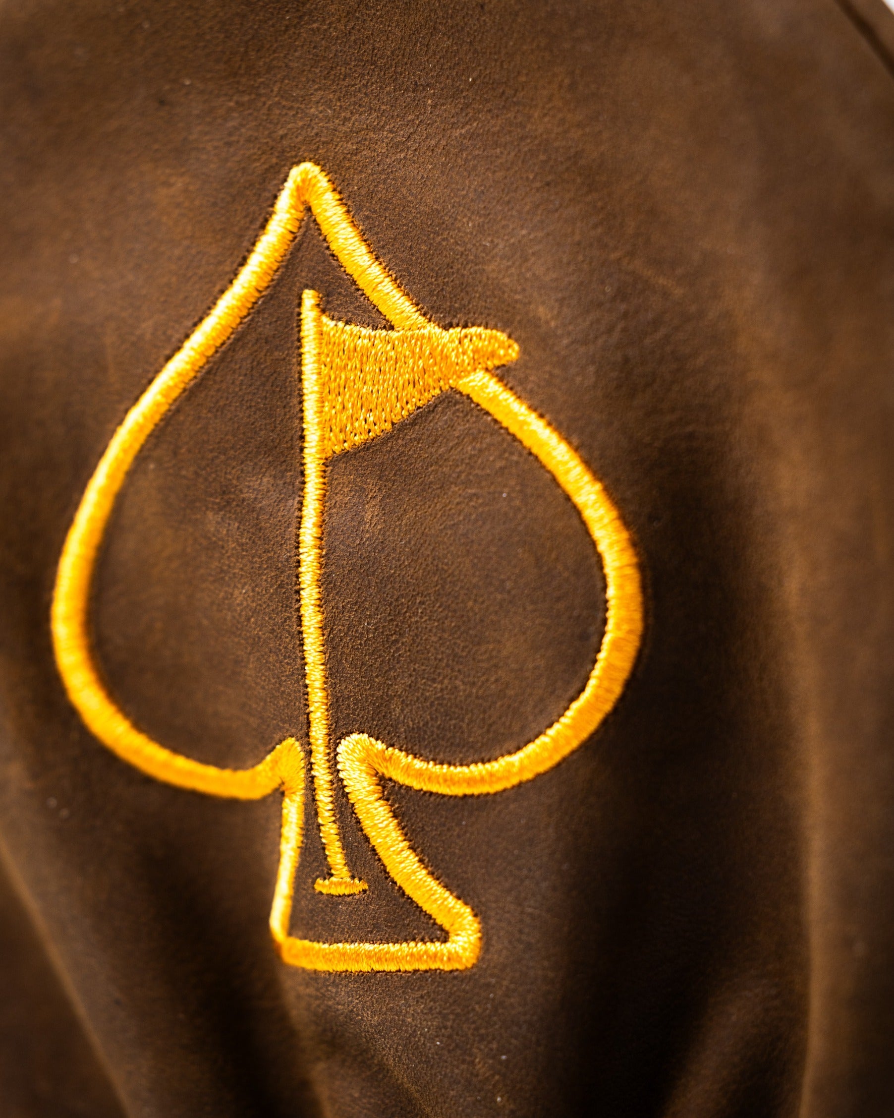 Brown driver cover featuring a bold yellow spade logo with a flag, designed for stylish golfers.