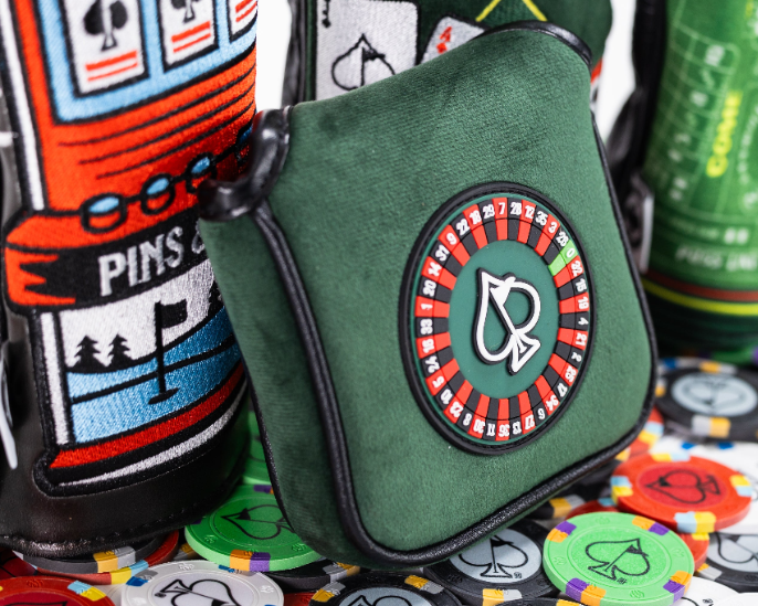 Green mallet putter cover featuring a roulette wheel design, surrounded by colorful poker chips and themed headcovers.