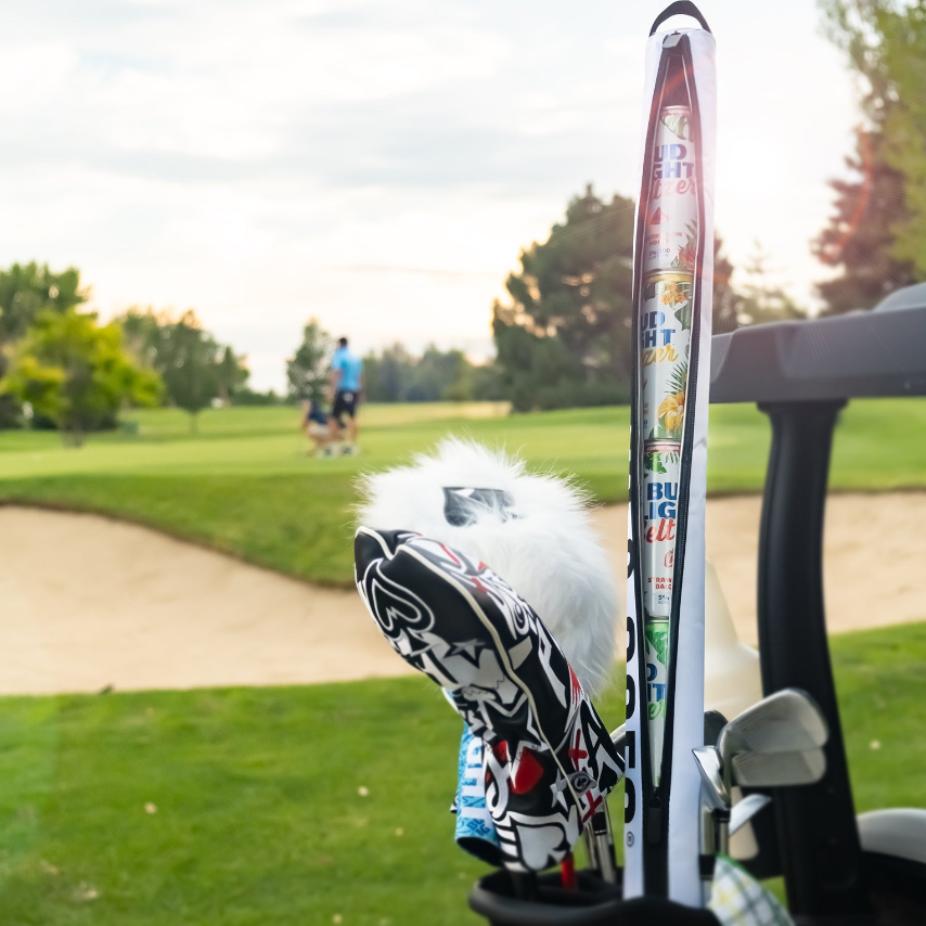 Seltzer sleeve attached to a golf bag, showcasing colorful designs while golfers play in the background on a sunny day.