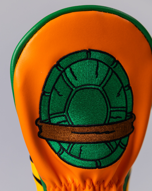 TMNT Michelangelo hybrid golf headcover featuring vibrant orange and green colors with a turtle shell design.