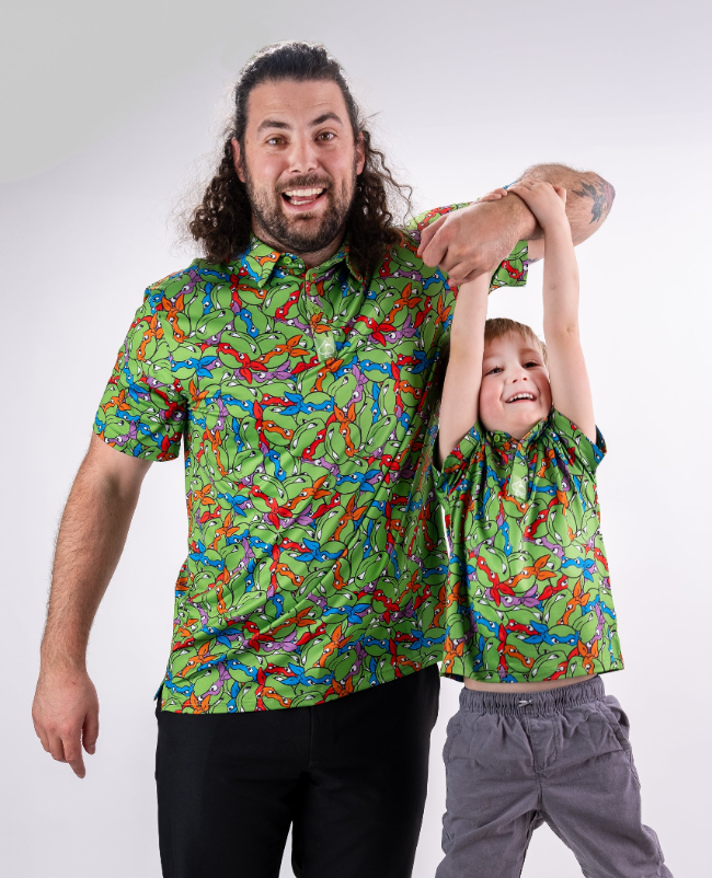 Father and son wearing matching TMNT shirts featuring vibrant green and colorful turtle designs, smiling and having fun.