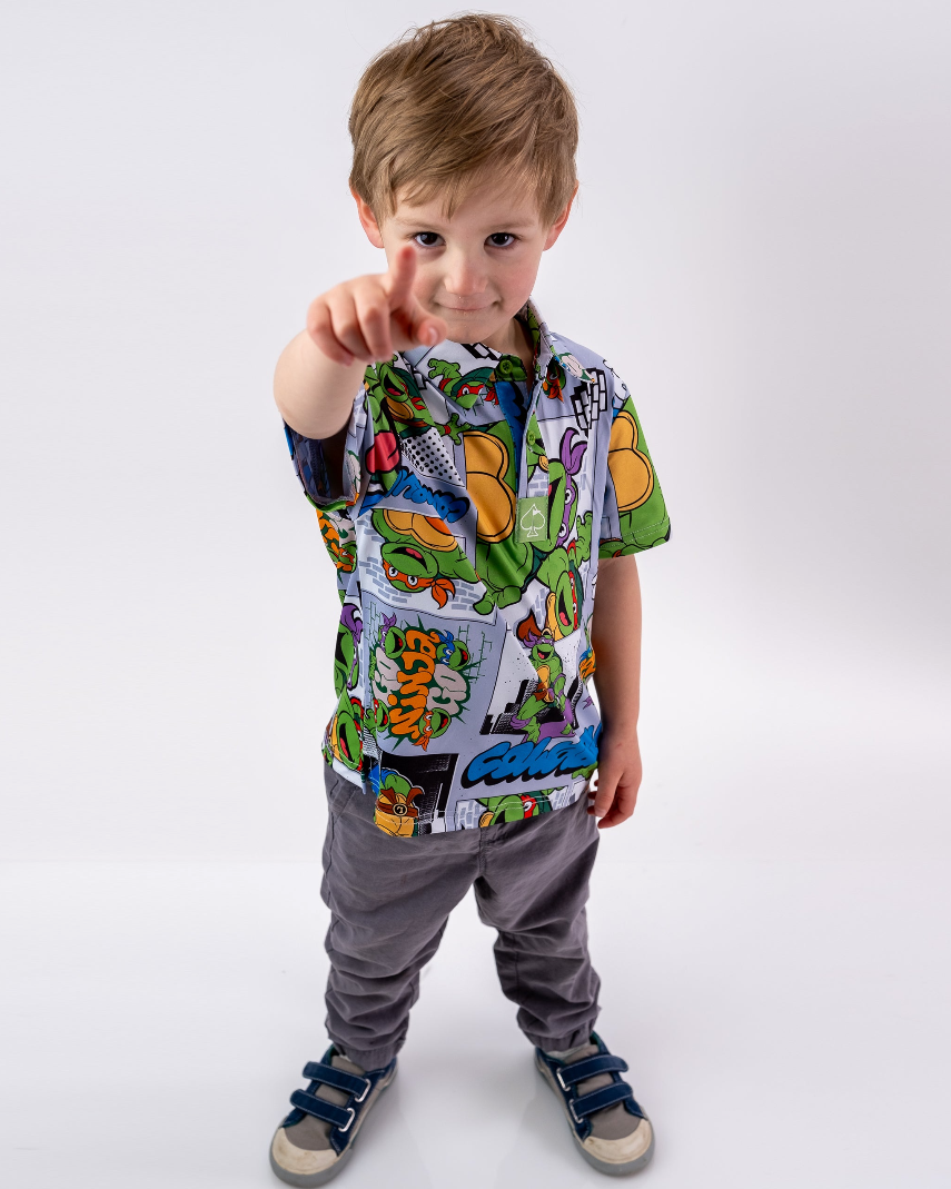 Youth in a colorful TMNT comic strip shirt points confidently, showcasing a fun and playful style perfect for young fans.