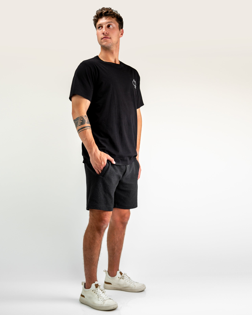Model wearing Player Preferred Waffleknit Shorts in Obsidian, paired with a black t-shirt and white sneakers, showcasing a casual style.