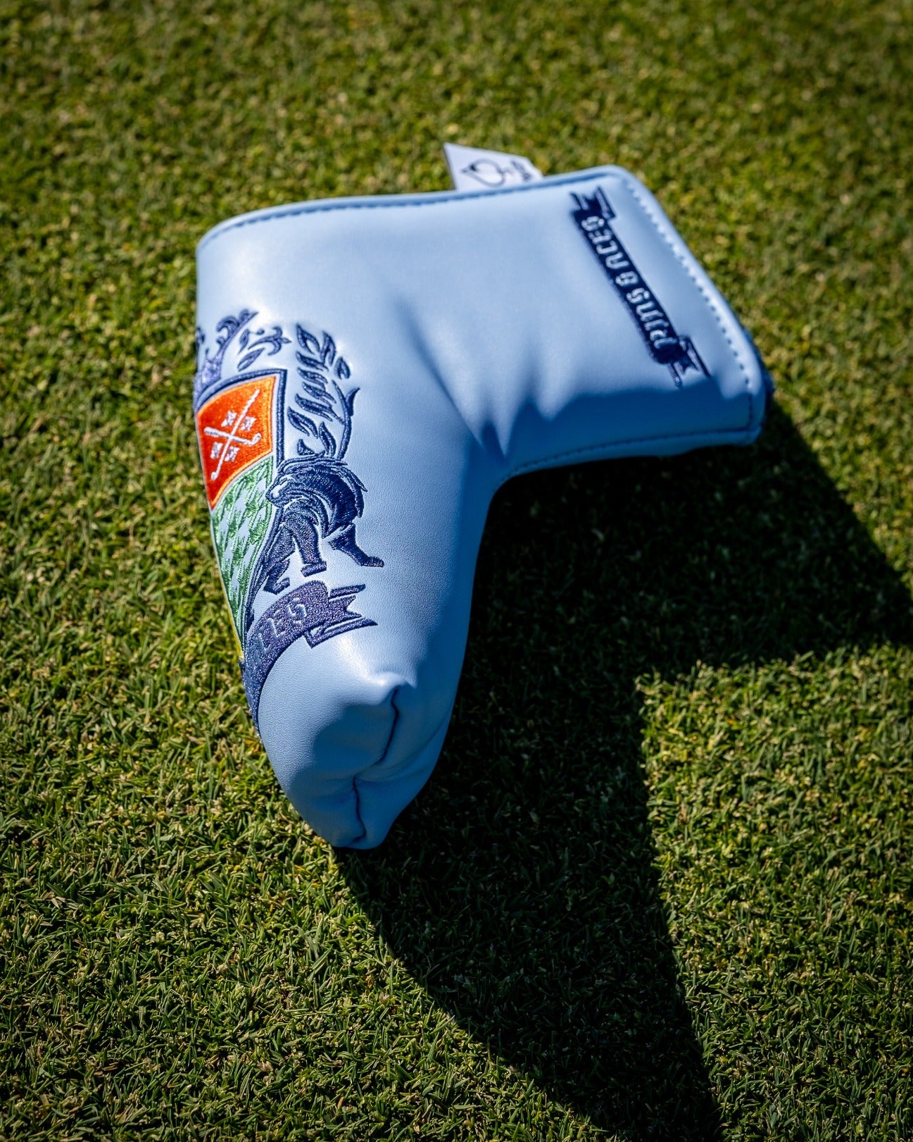Blade putter cover featuring a colorful coat of arms design on a light blue background, ideal for stylish golfers.